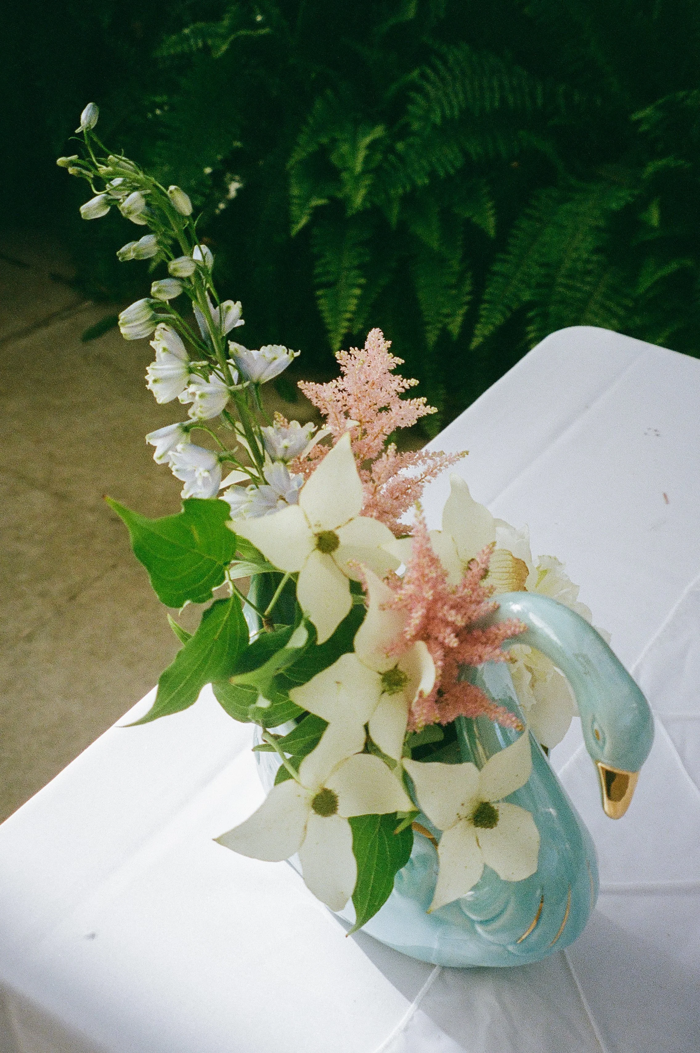 Close-up of floral arrangement with soft pastel blooms arranged in a swan-shaped vase, styled for film wedding photography