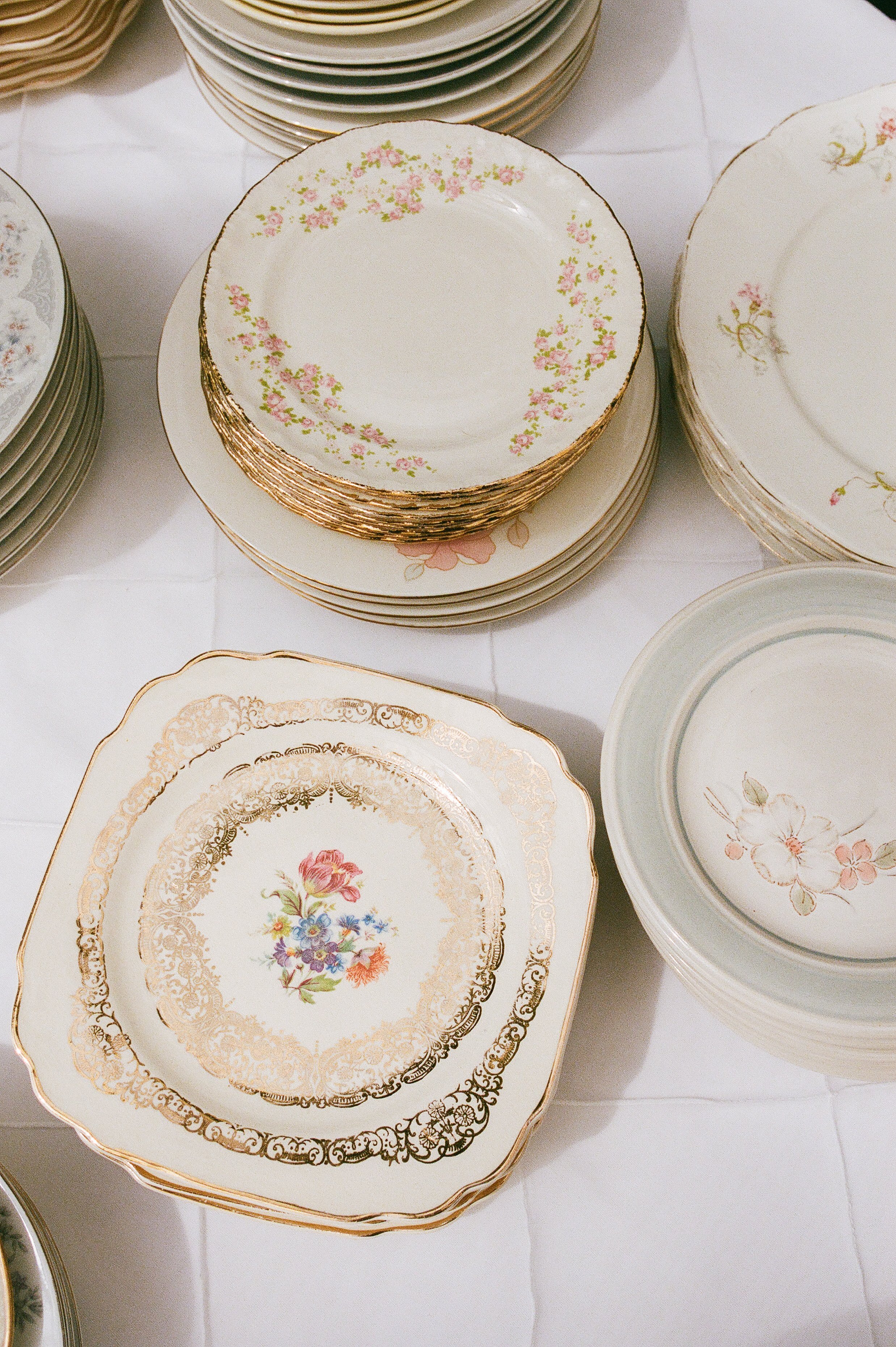 Vintage floral china plates with gold detailing arranged on a table, styled for a romantic film wedding photography aesthetic