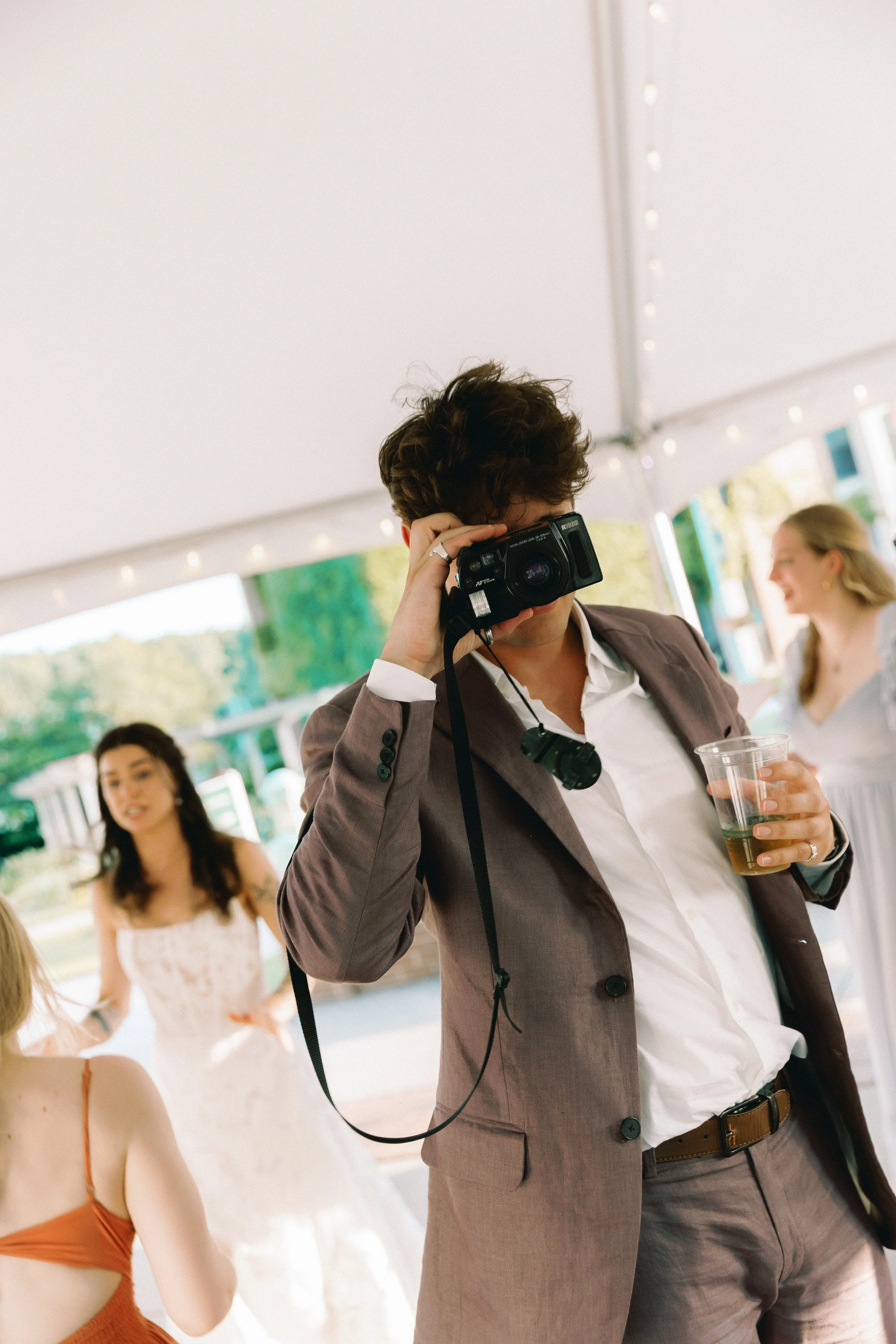 Guest taking a candid photo with a camera while holding a drink during the reception