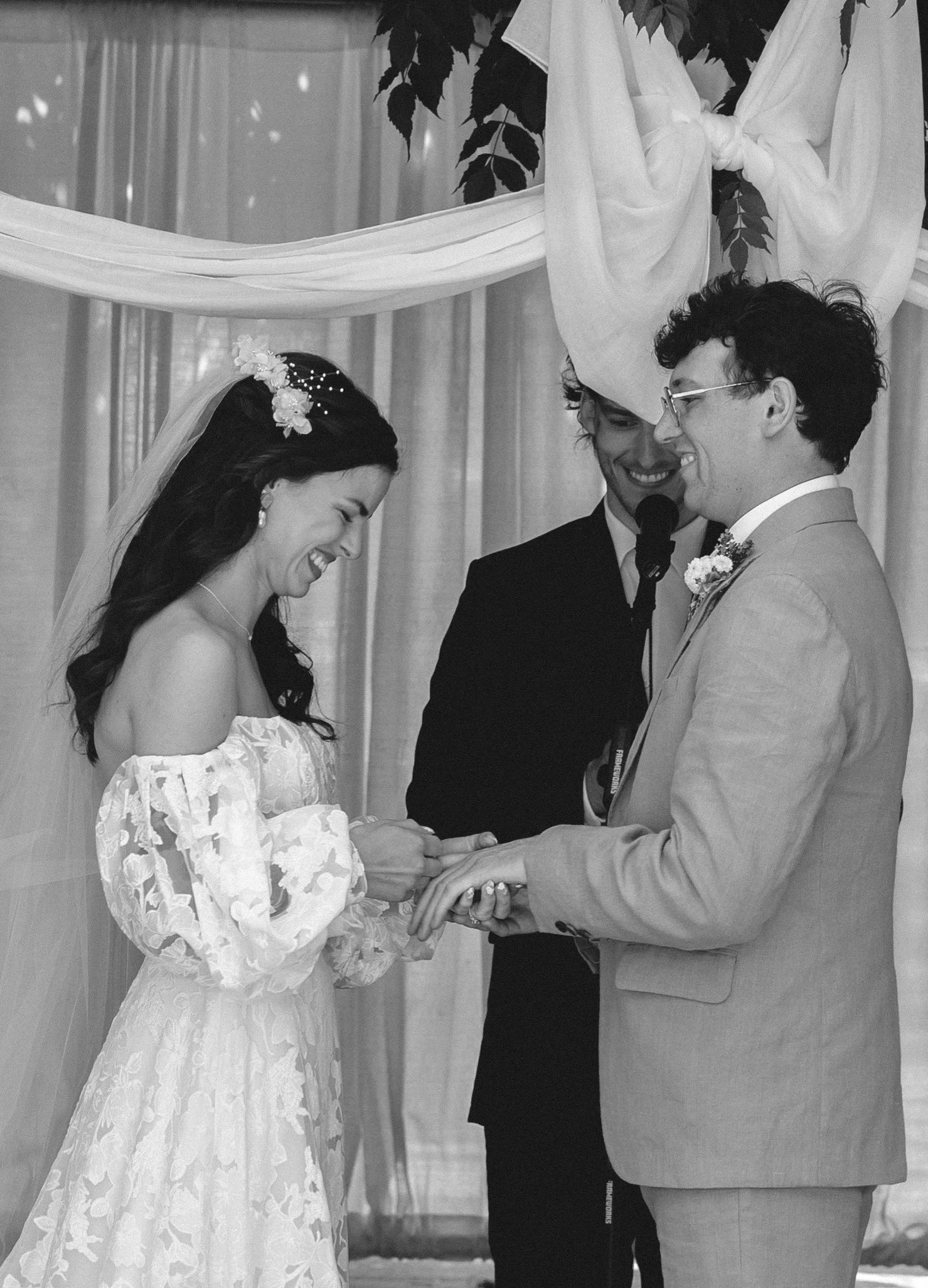 Bride and groom exchanging rings during their ceremony, smiling at each other in an intimate black and white frame