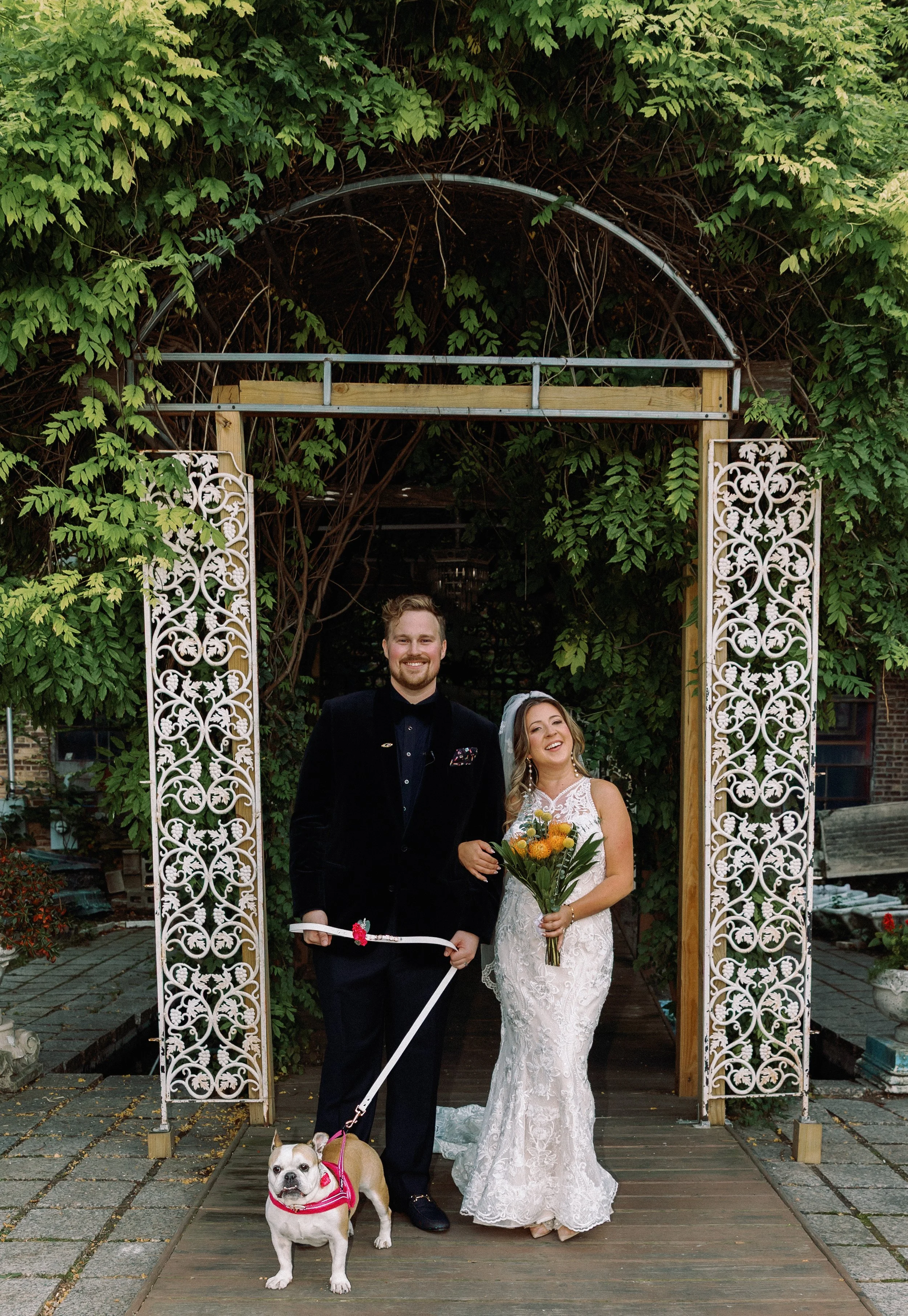 Newlywed couple posing under a vine-covered arch with their dog after their Salvage One wedding
