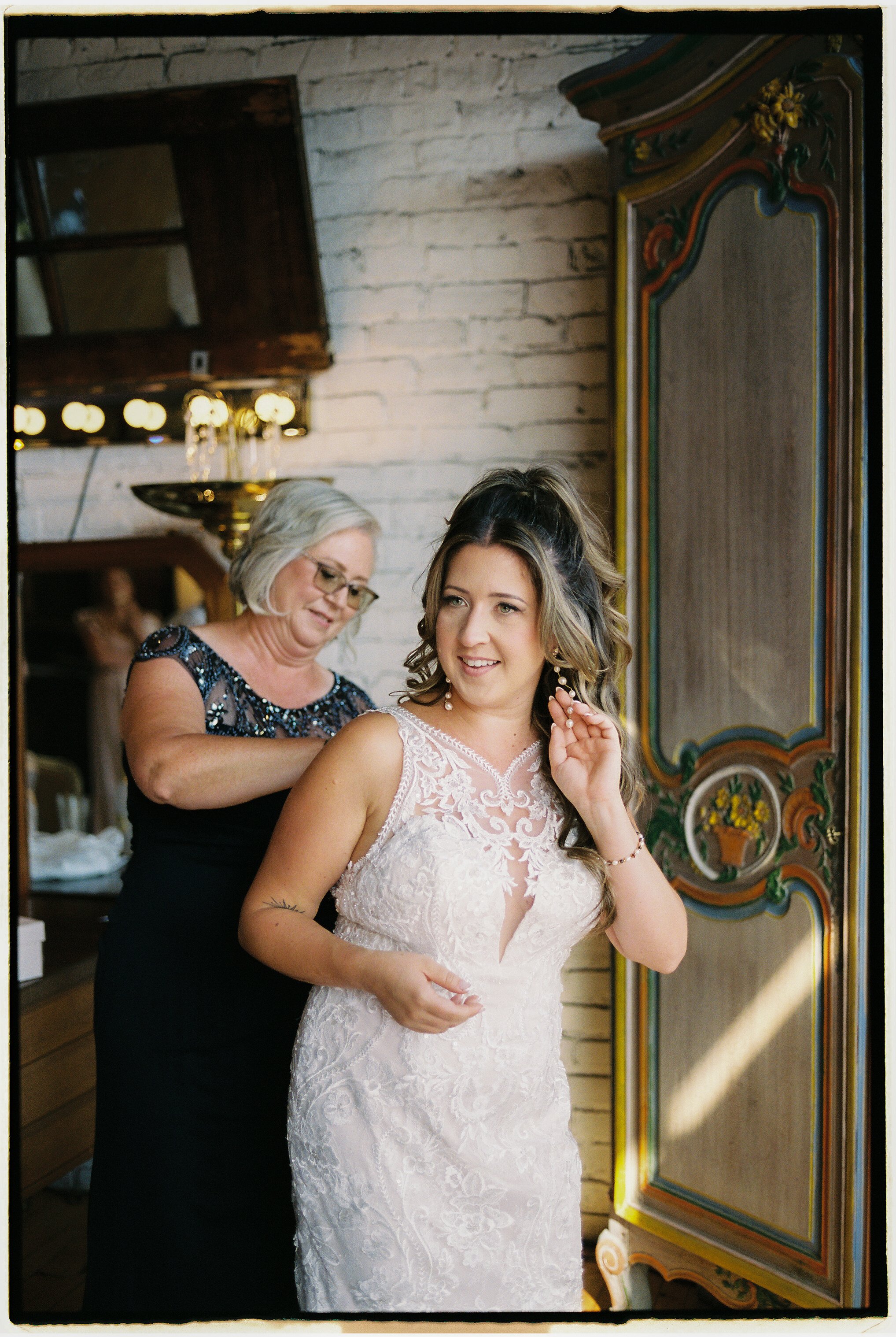 Bride getting ready with help fastening her dress in a softly lit vintage bridal suite