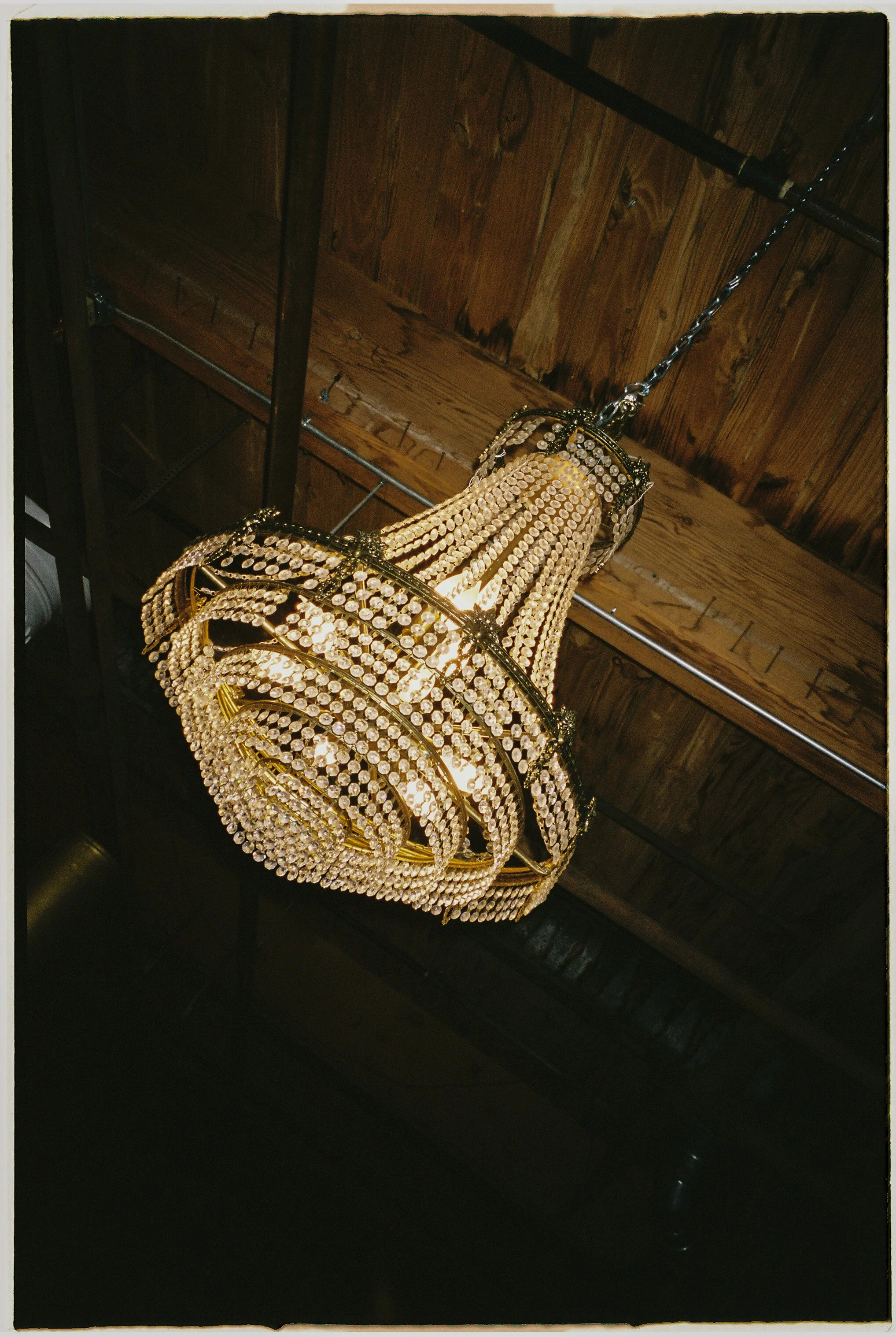 Vintage crystal chandelier hanging from wooden ceiling beams at Salvage One