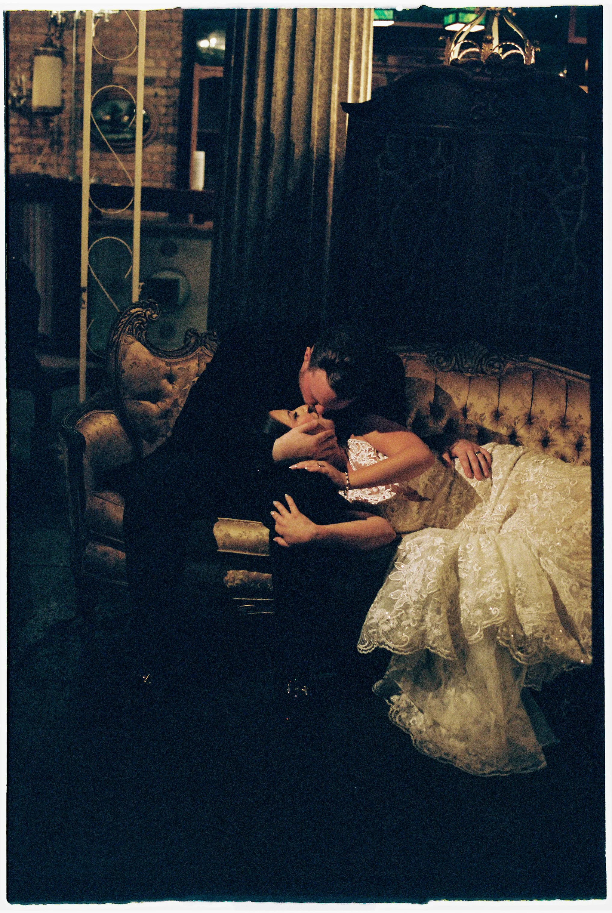 Couple sharing an intimate kiss on a vintage couch in a dimly lit Salvage One space