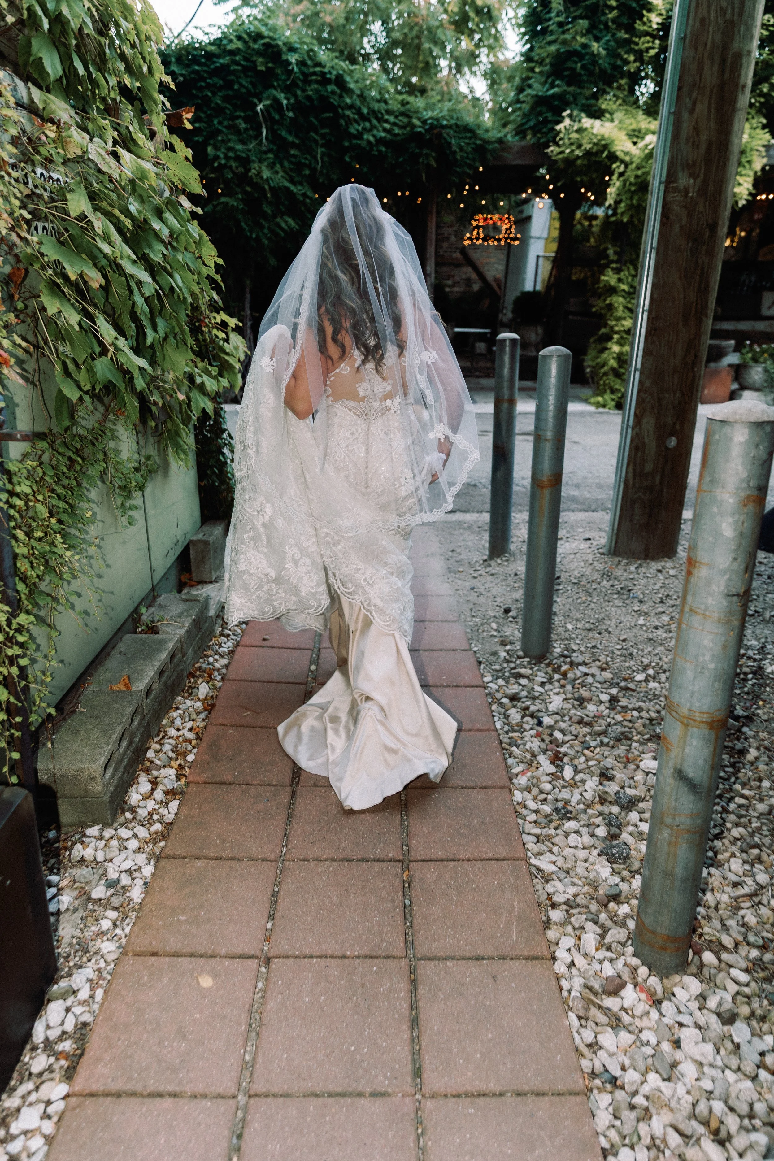 Bride walking down a garden pathway in her gown and veil at Salvage One courtyard