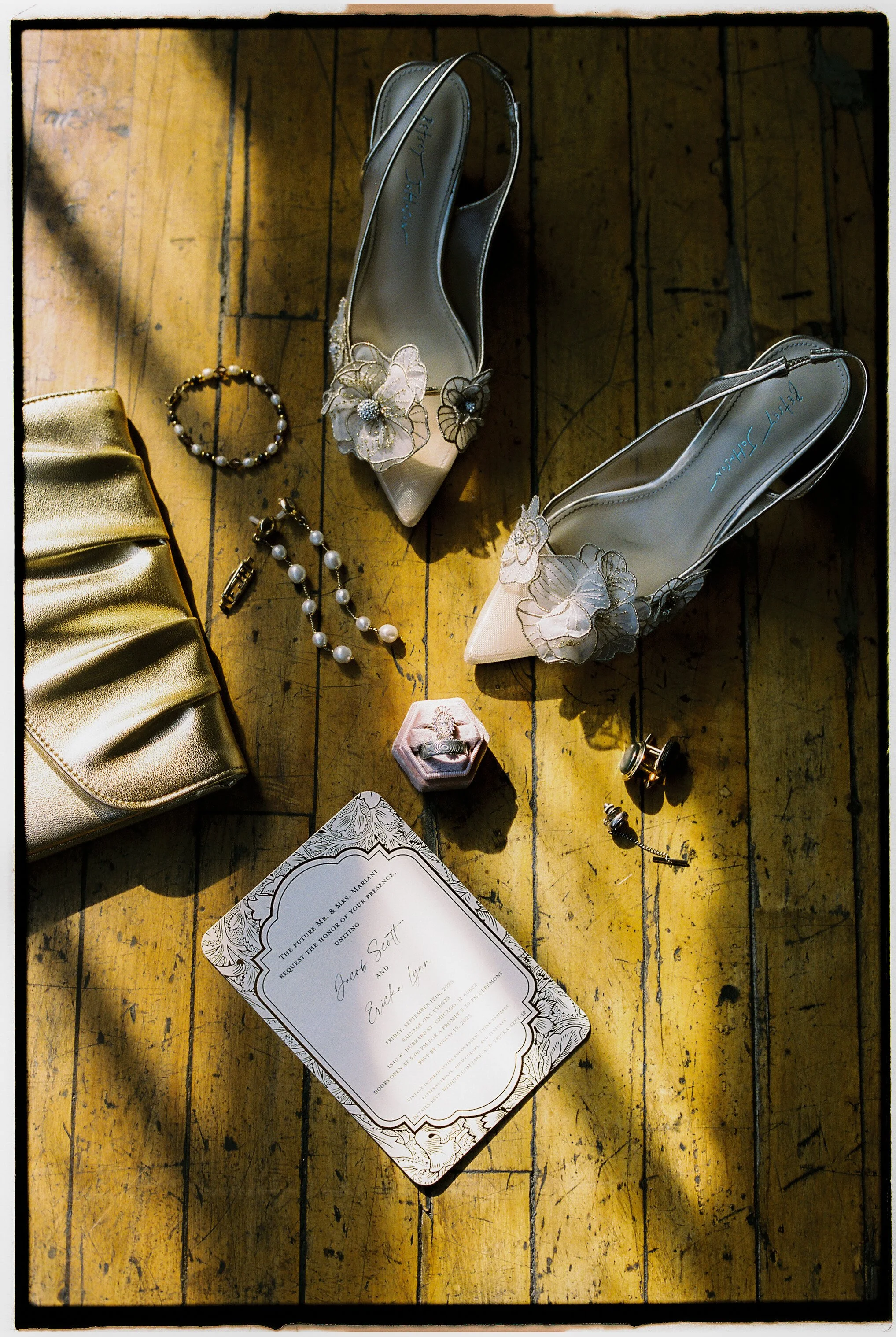 Bridal details including floral heels, jewelry, and invitation suite styled on wooden floor