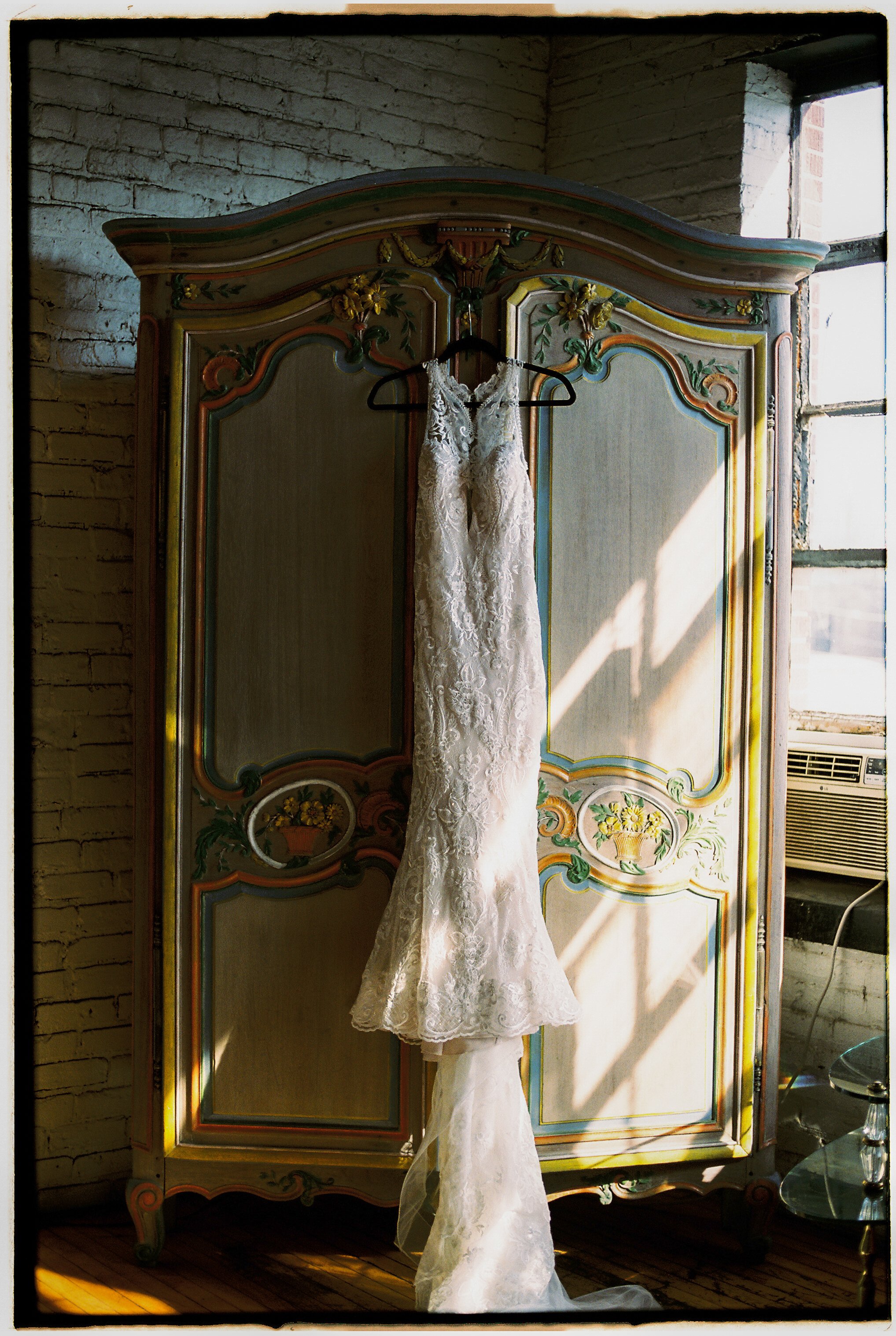 Wedding dress hanging on a painted vintage armoire in natural window light at Salvage One