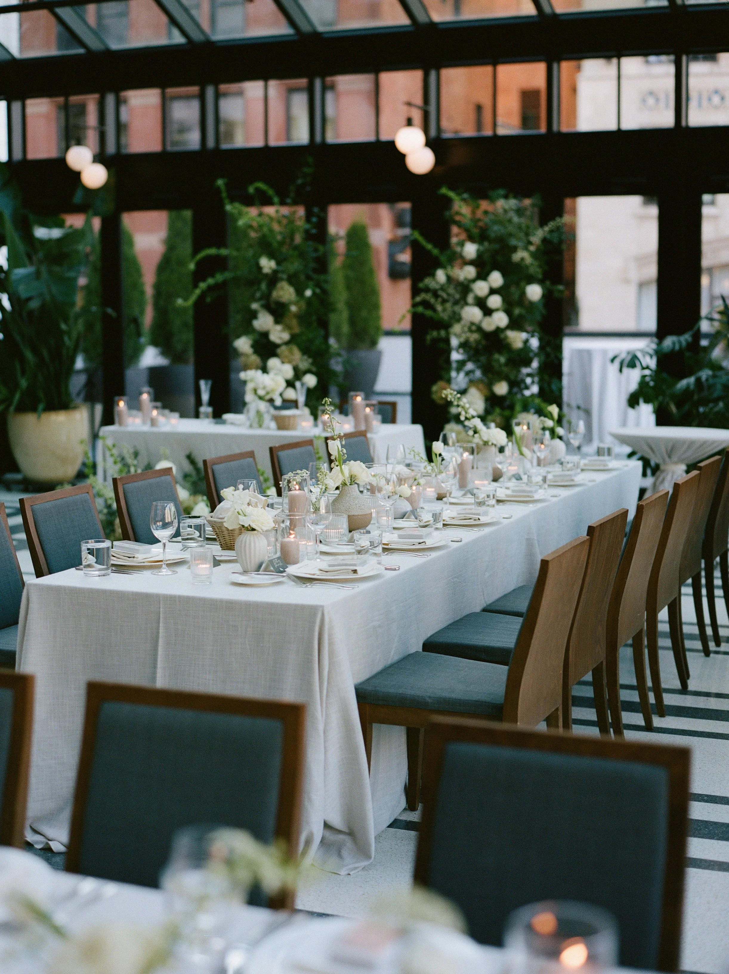 Long reception tables with candles, neutral linens, and floral arrangements set inside Shinola Hotel’s glass atrium event space