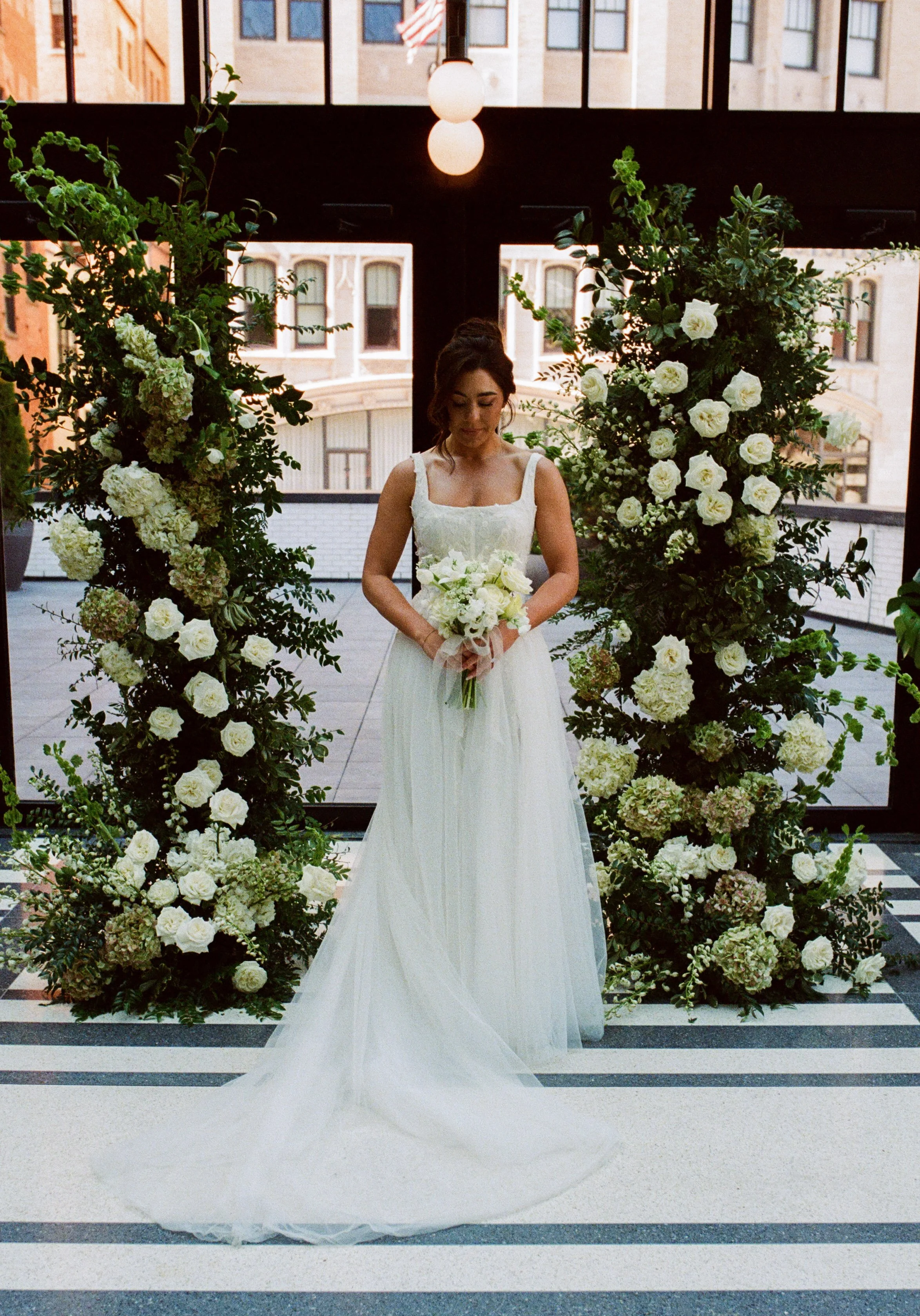 Bride standing between lush white and green floral ceremony installations during a Shinola Hotel wedding