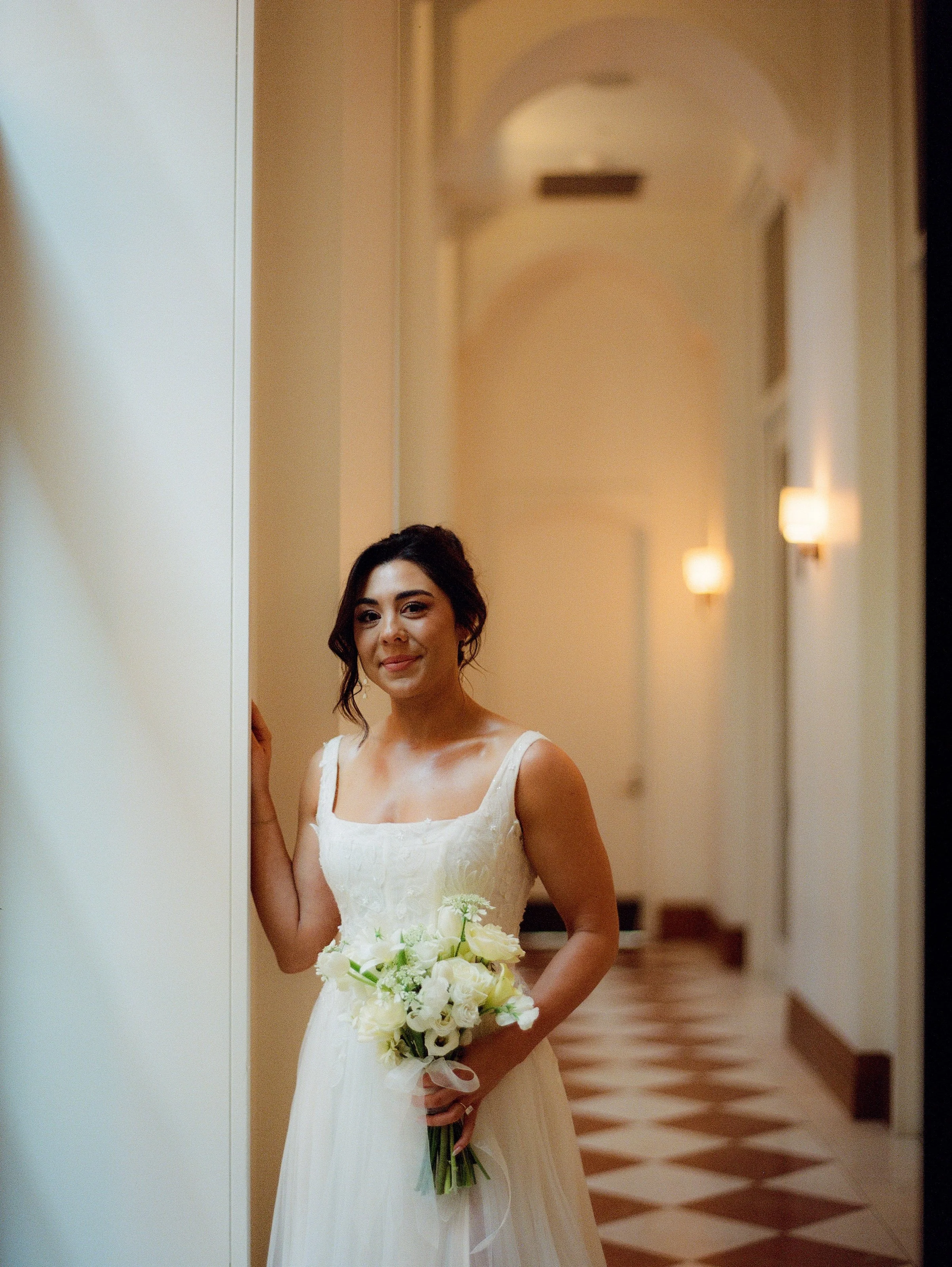 Bride holding a white bouquet while standing in the arched hallway inside Shinola Hotel