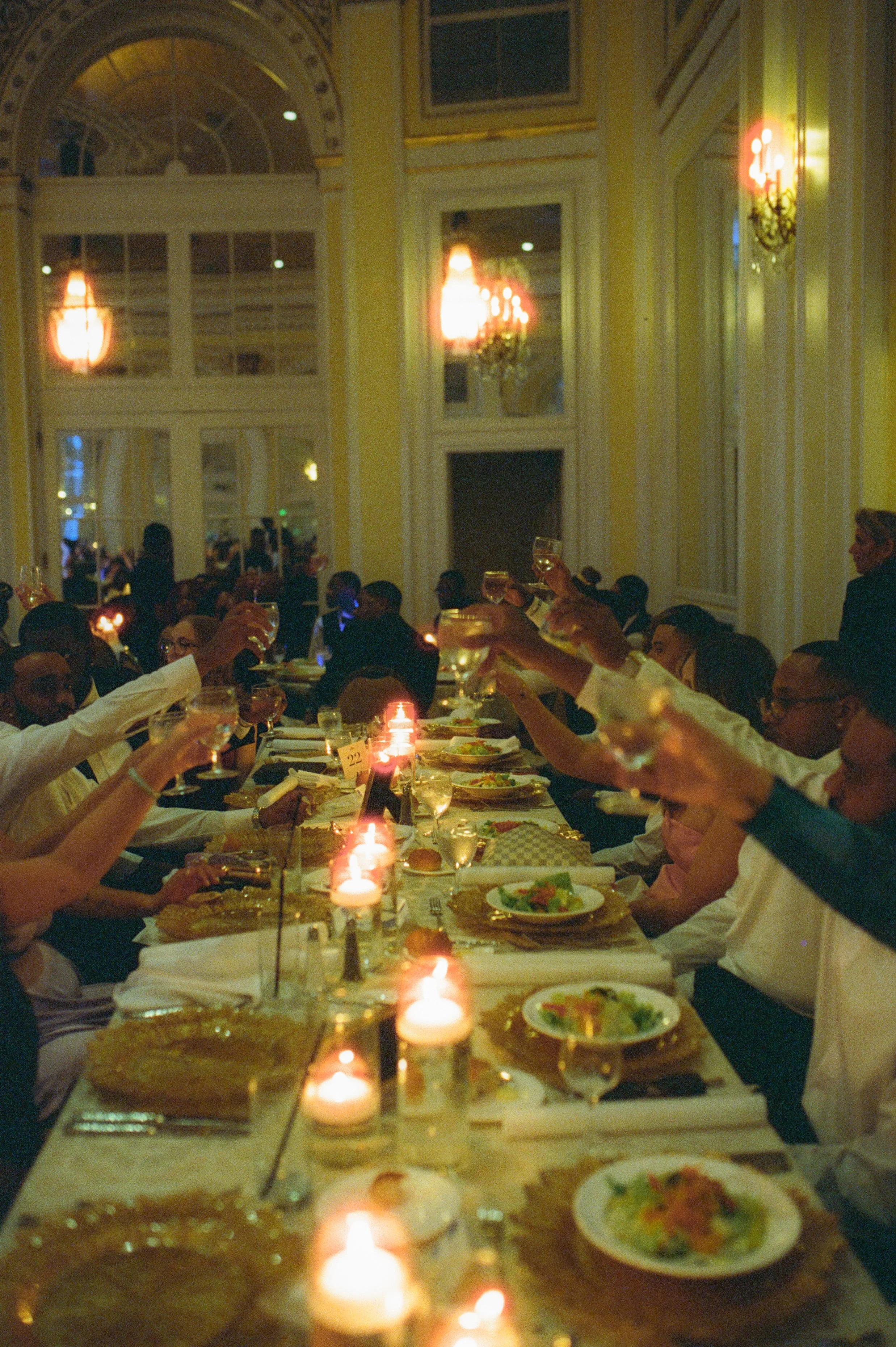 Guests raising glasses during a candlelit wedding dinner in an elegant ballroom with cinematic film photography style