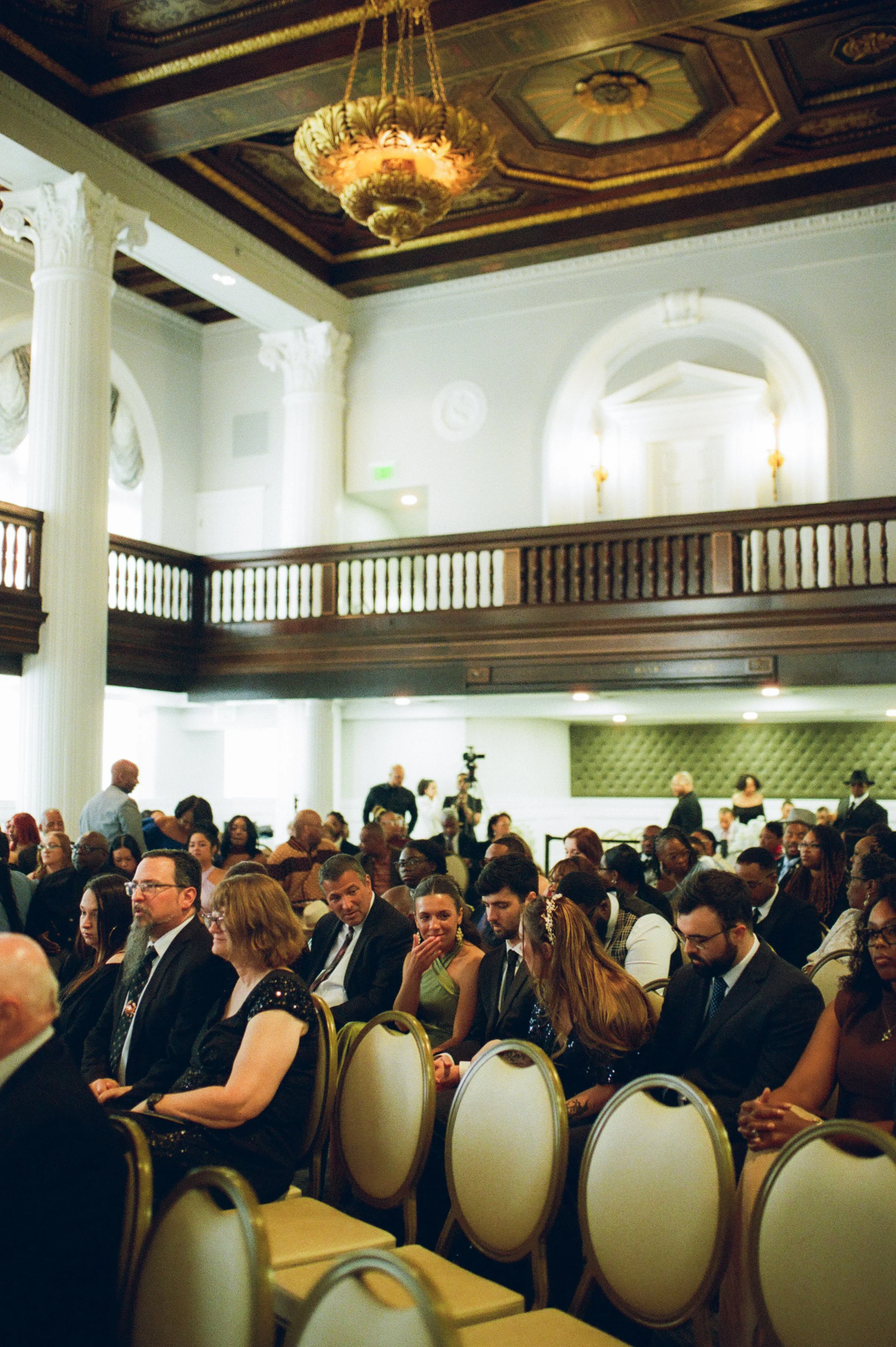 Guests seated inside a historic ballroom waiting for the wedding ceremony to begin captured in cinematic film photography style
