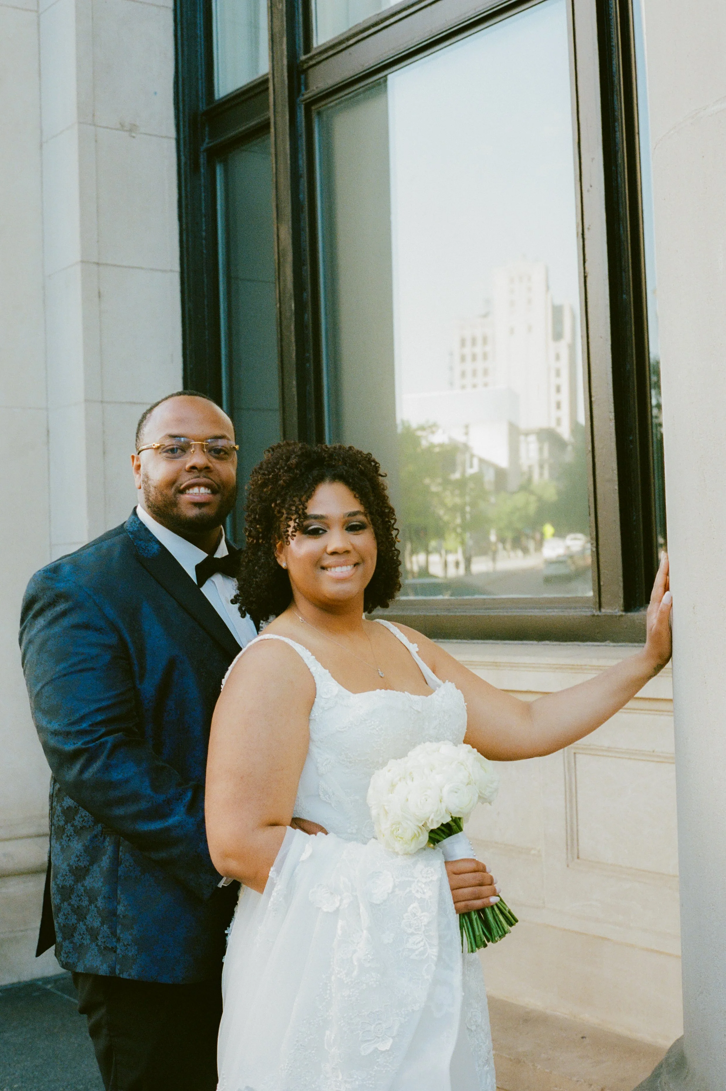 Romantic wedding portrait of the bride and groom outside a historic downtown hotel with white roses and soft evening light