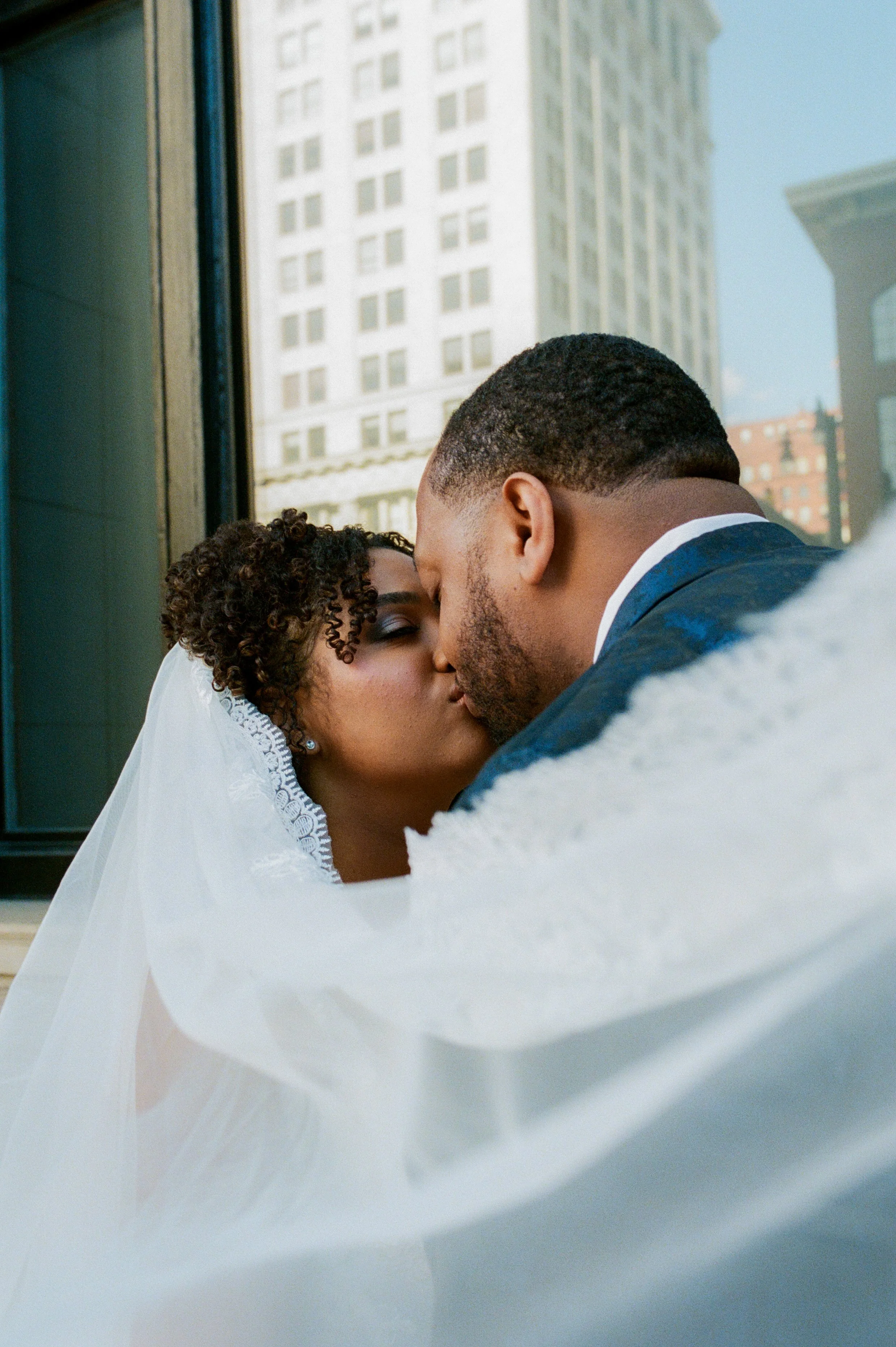 Close-up portrait of the bride and groom kissing beneath the bride’s veil outside a downtown wedding venue