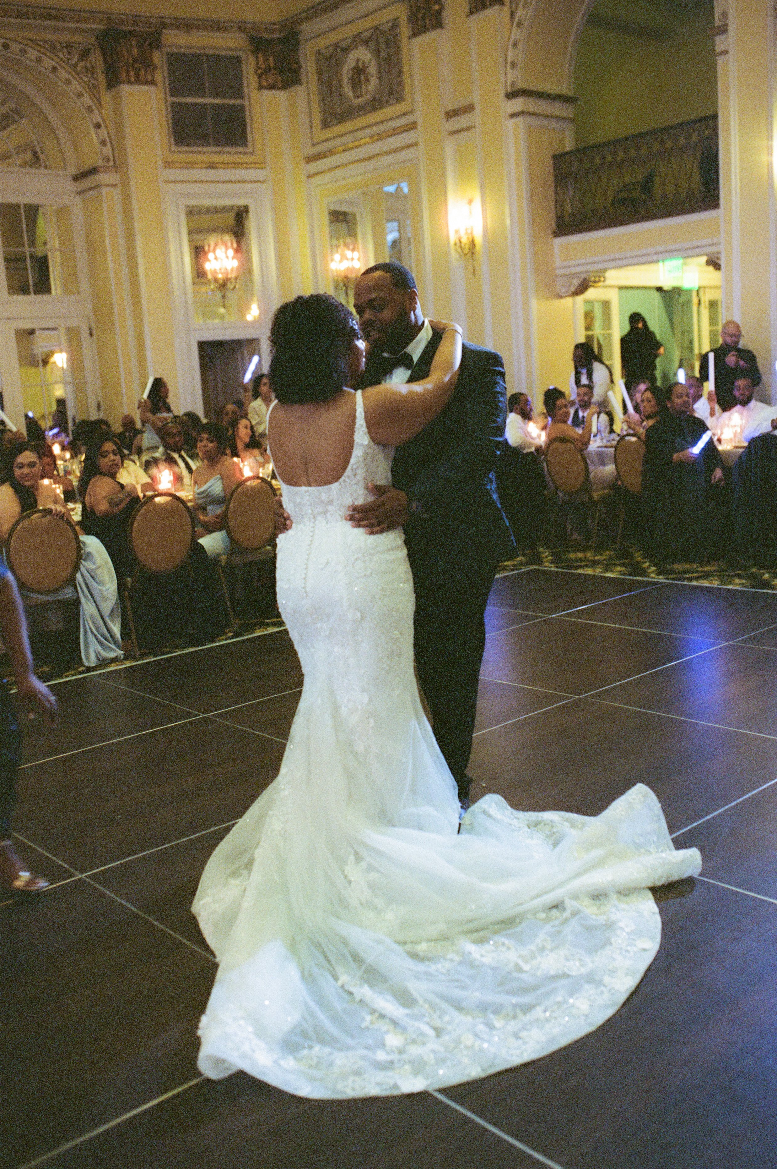 Bride and groom sharing their first dance in a grand reception hall with a flowing lace wedding dress