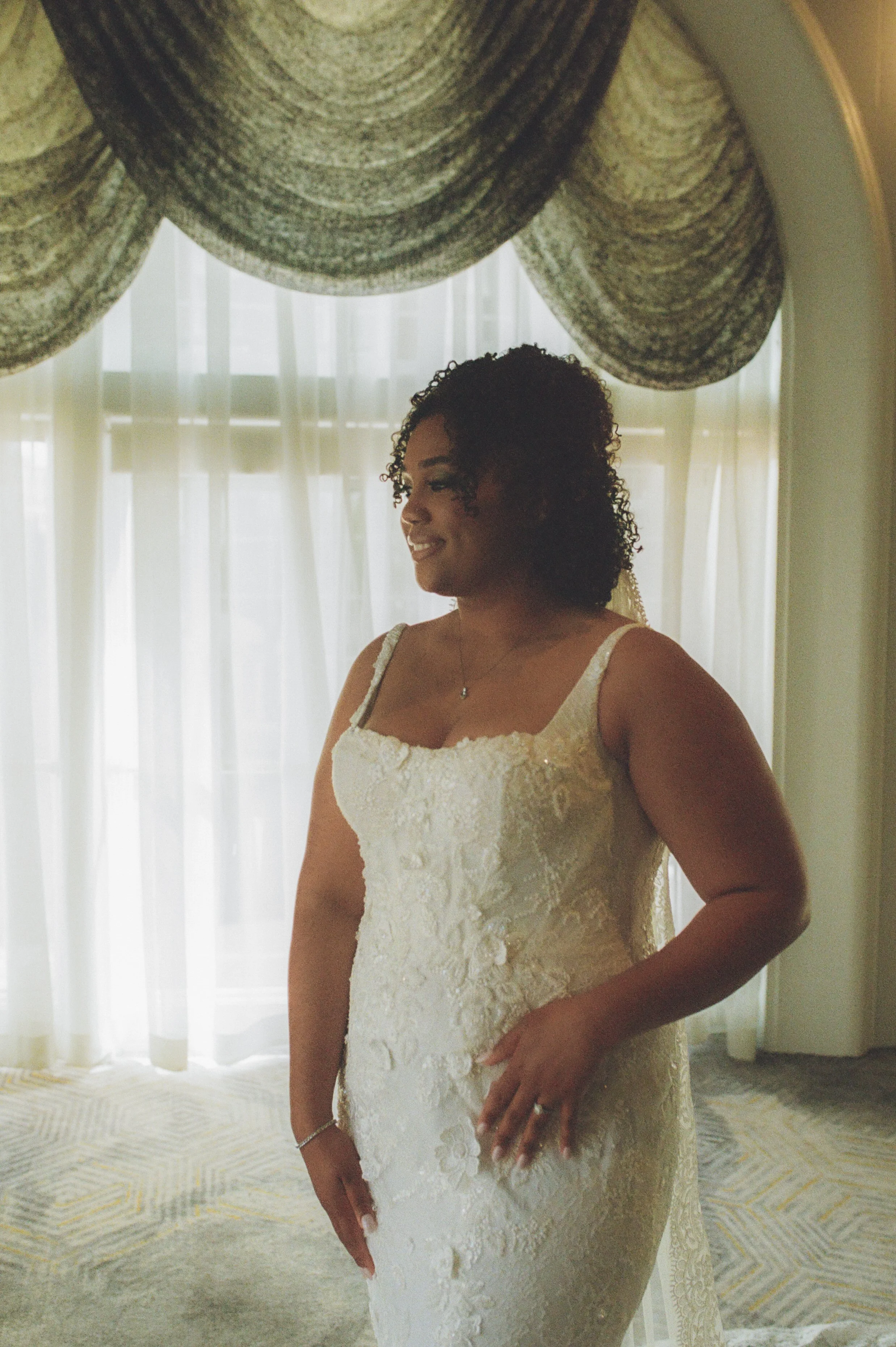 Bridal portrait beside softly lit windows in a historic ballroom with cinematic film photography tones