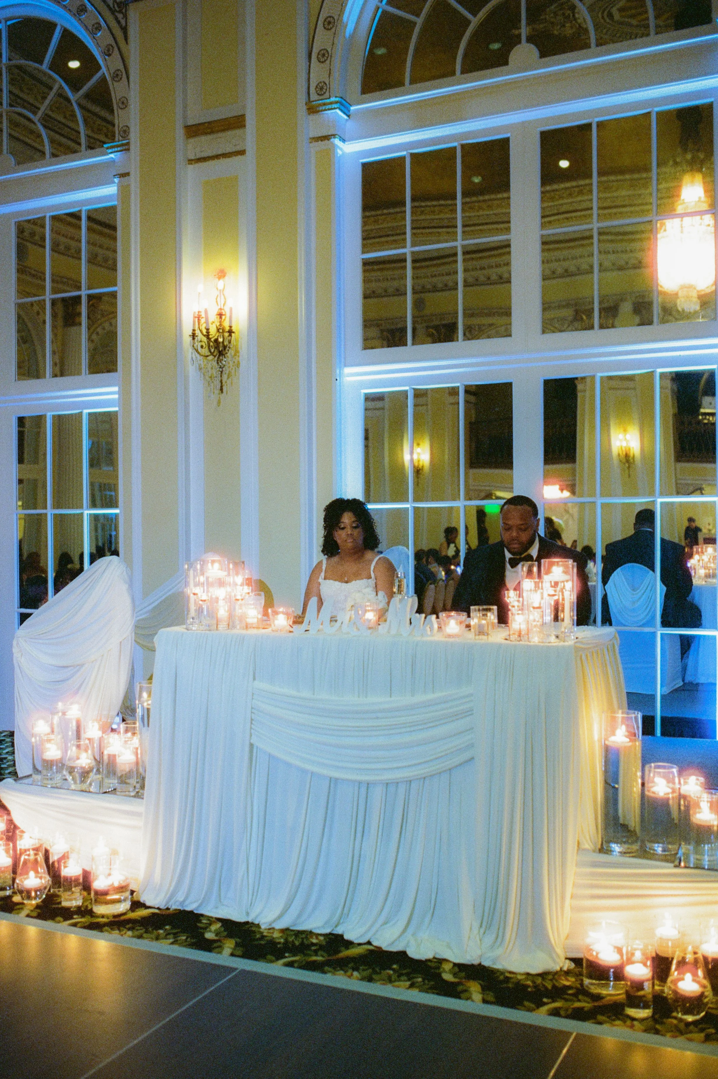 Bride and groom sitting at their sweetheart table surrounded by candle light