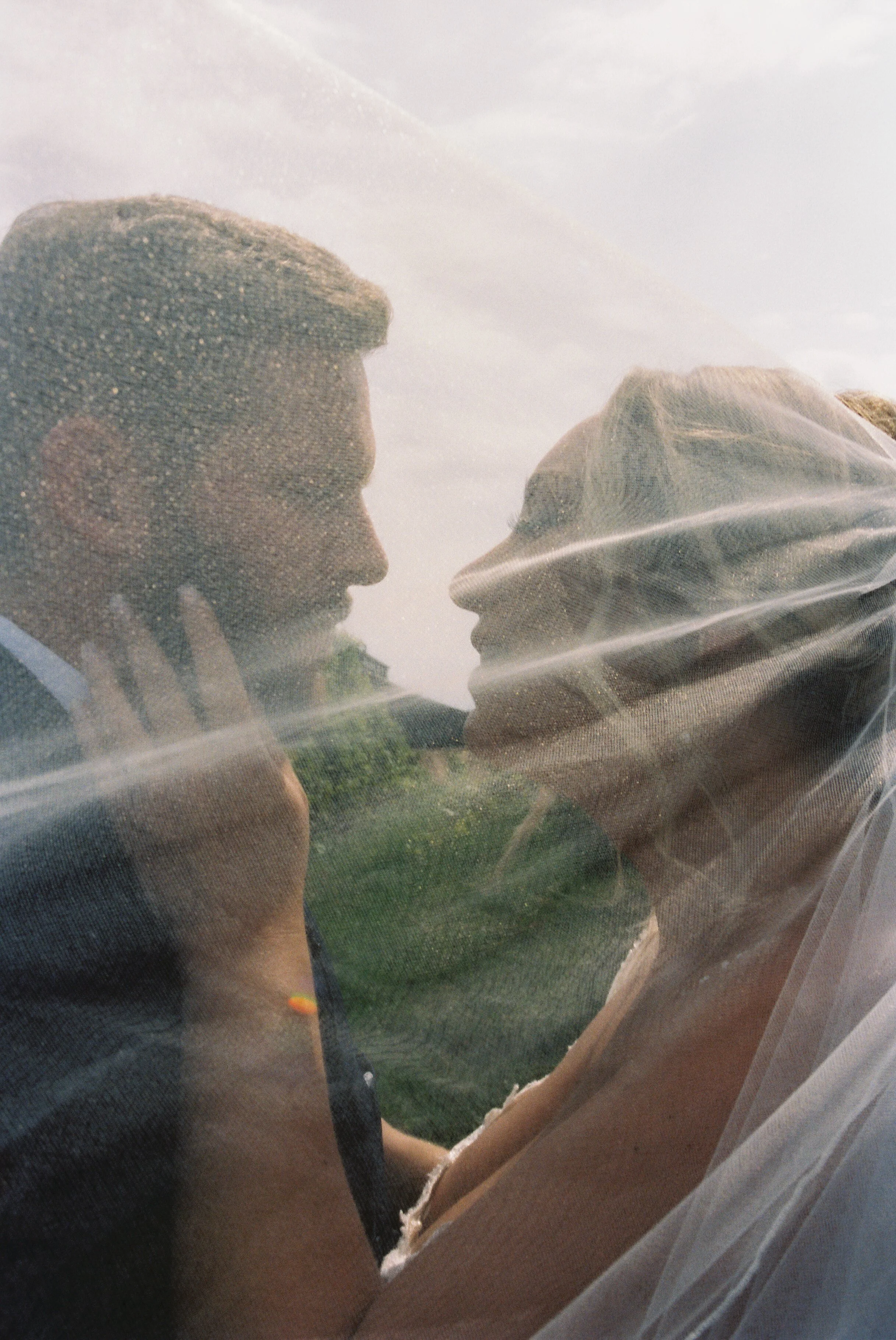 Romantic close-up portrait of a newlywed couple wrapped in a veil with soft sunlight filtering through during a Northern Michigan vineyard wedding.
