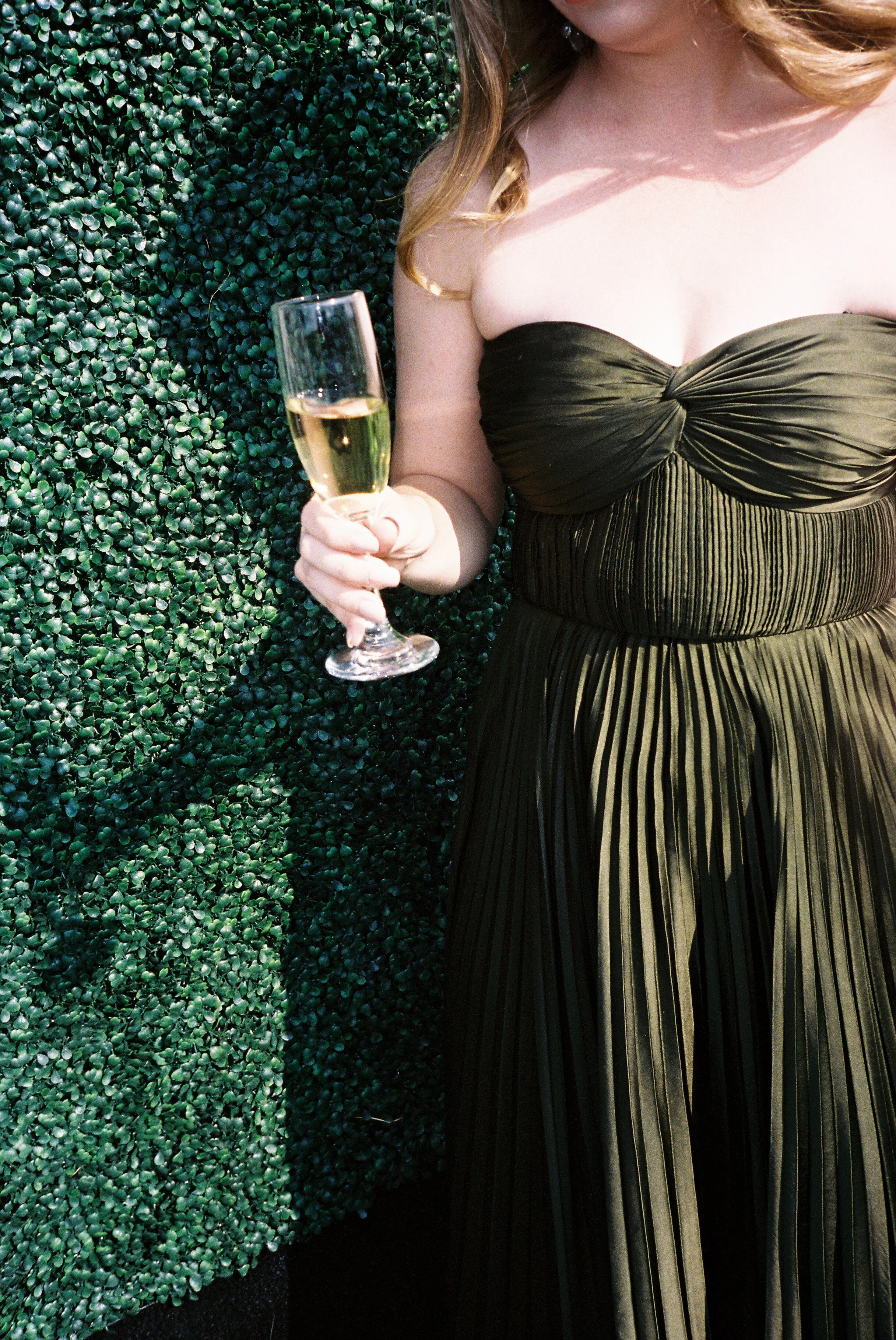 Wedding guest holding a champagne flute while wearing a black pleated dress at an outdoor Northern Michigan vineyard wedding cocktail hour.