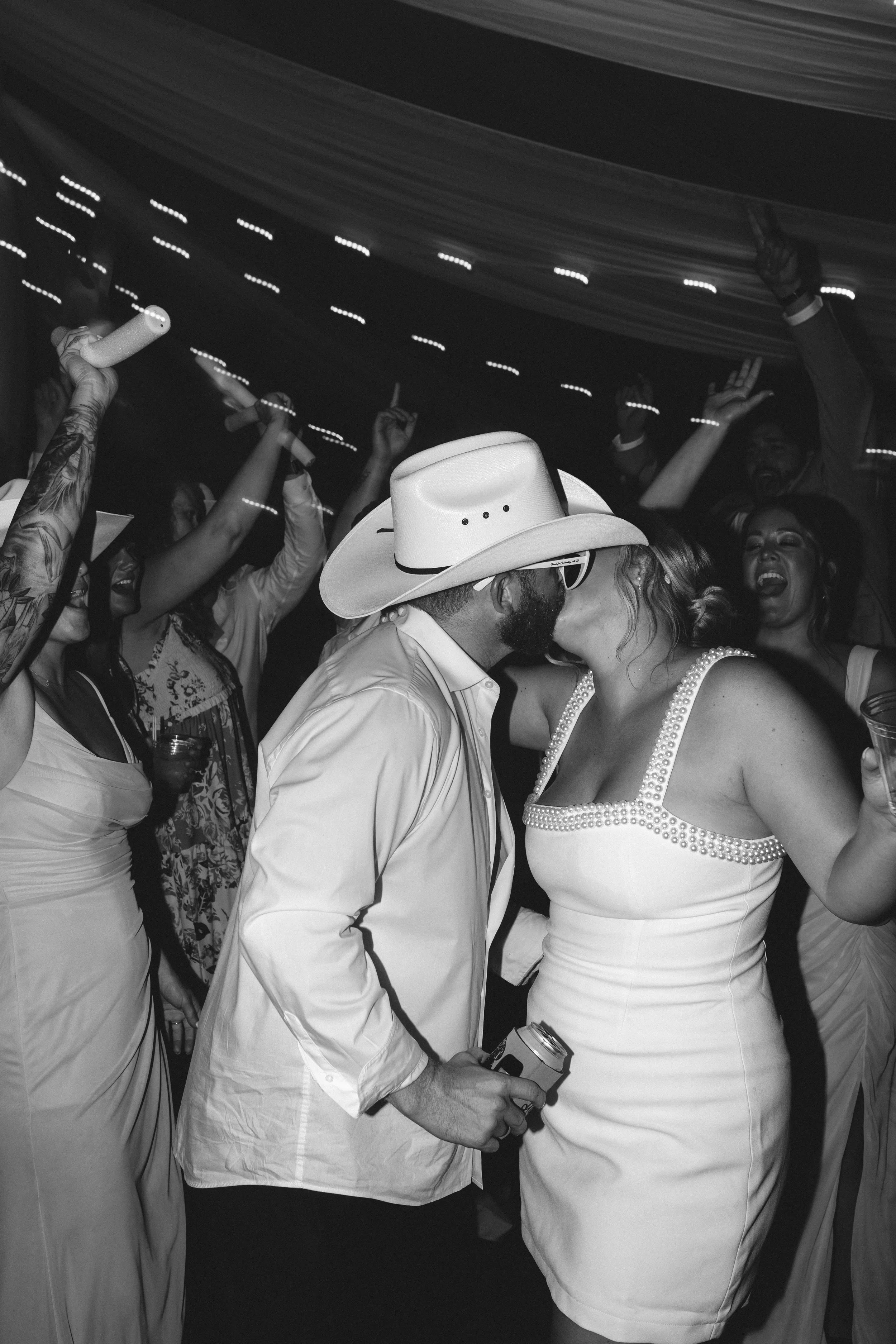 Bride and groom sharing a kiss on a packed dance floor as guests celebrate around them during their wedding reception.
