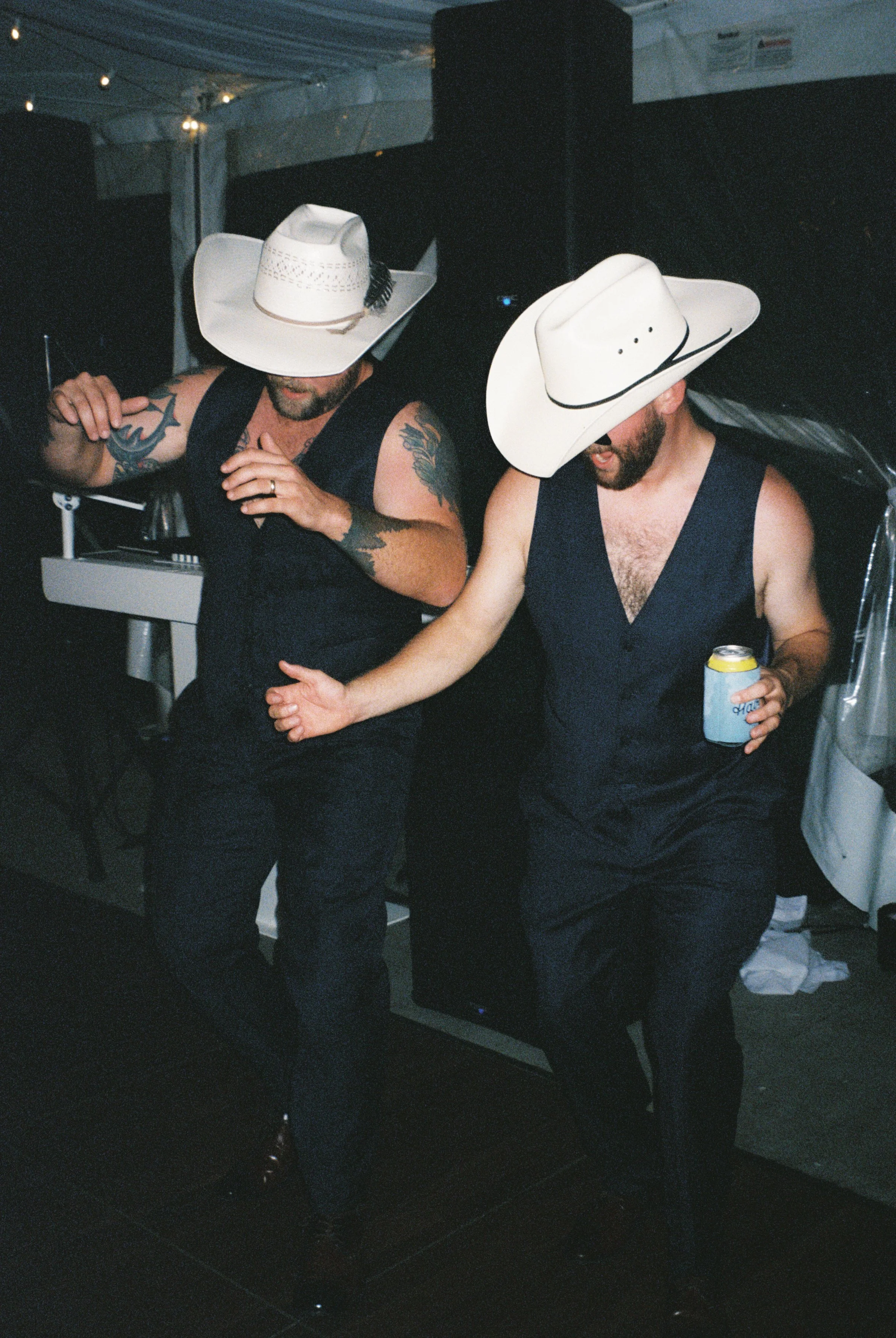 Two wedding guests dancing in cowboy hats during a lively reception celebration.