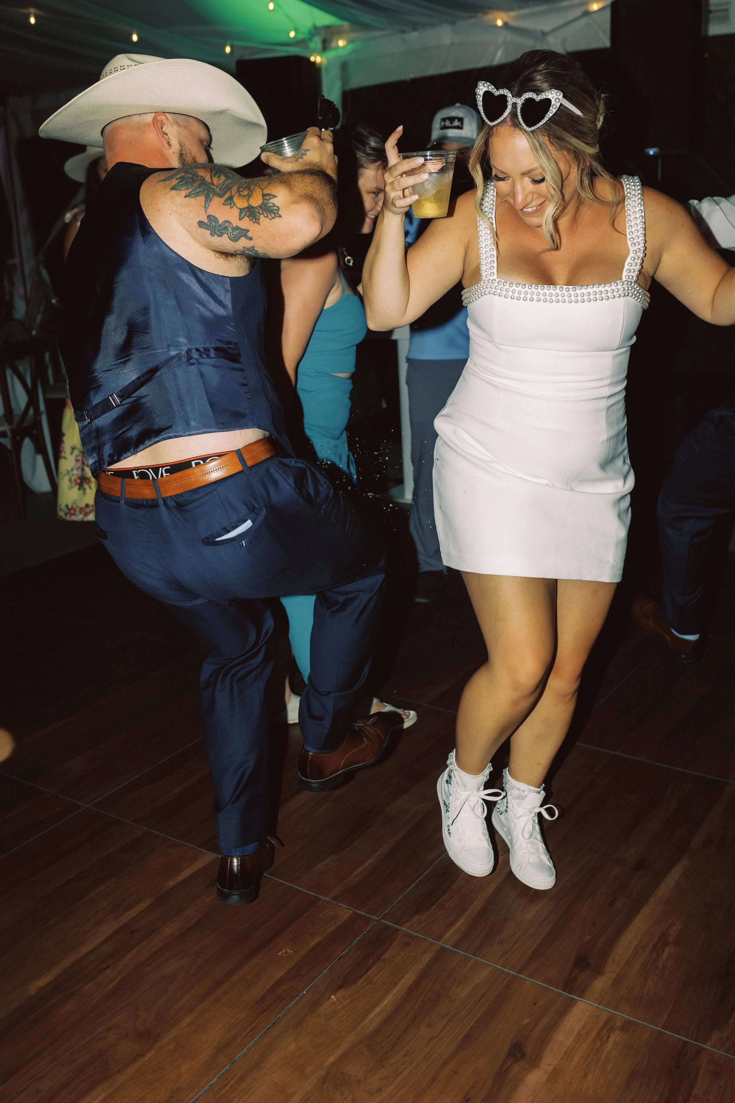 Bride dancing in a short reception dress and sneakers while celebrating with guests on the dance floor.