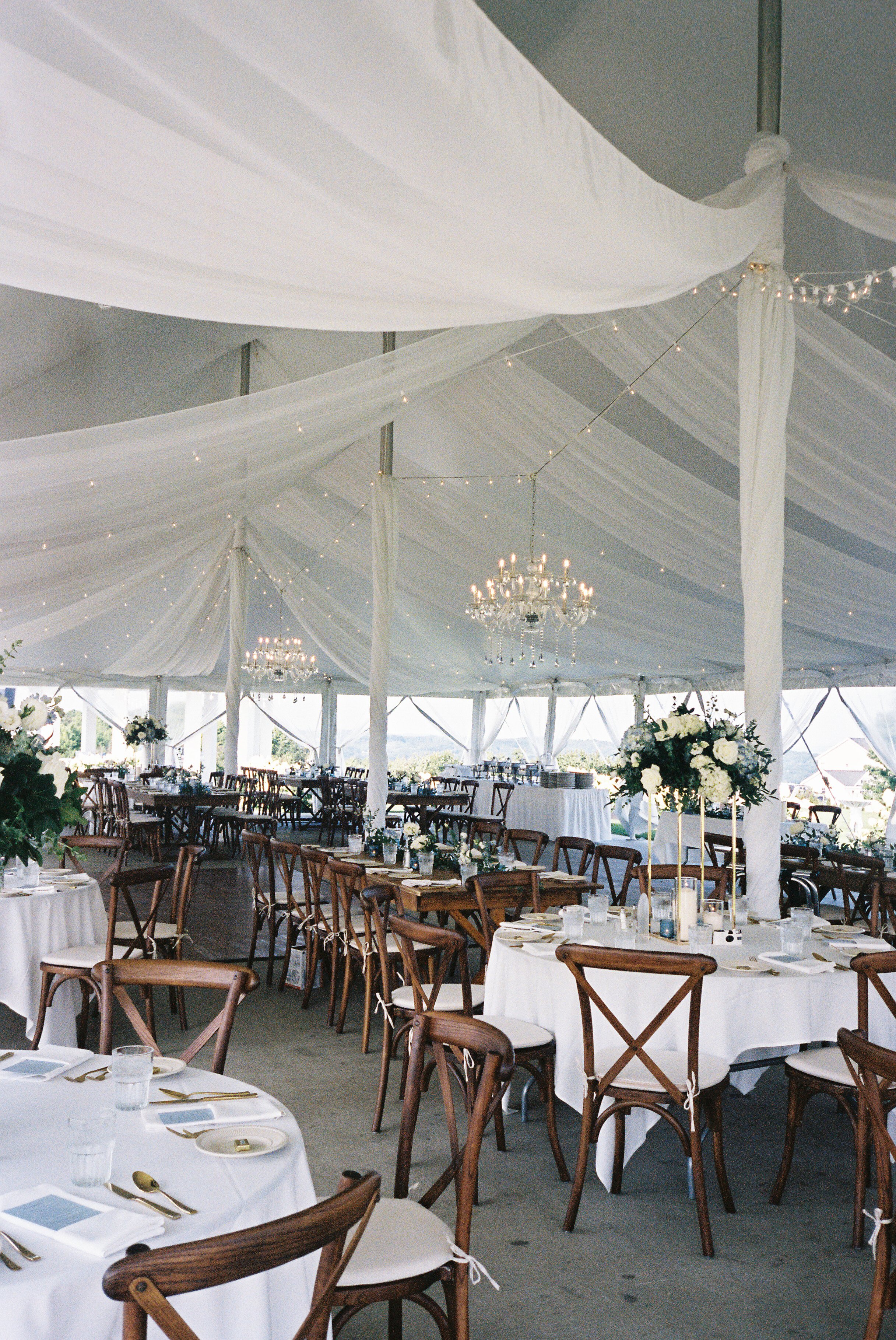 Elegant wedding reception tent with draped white fabric, chandeliers, and round tables set for guests at a Northern Michigan vineyard wedding.