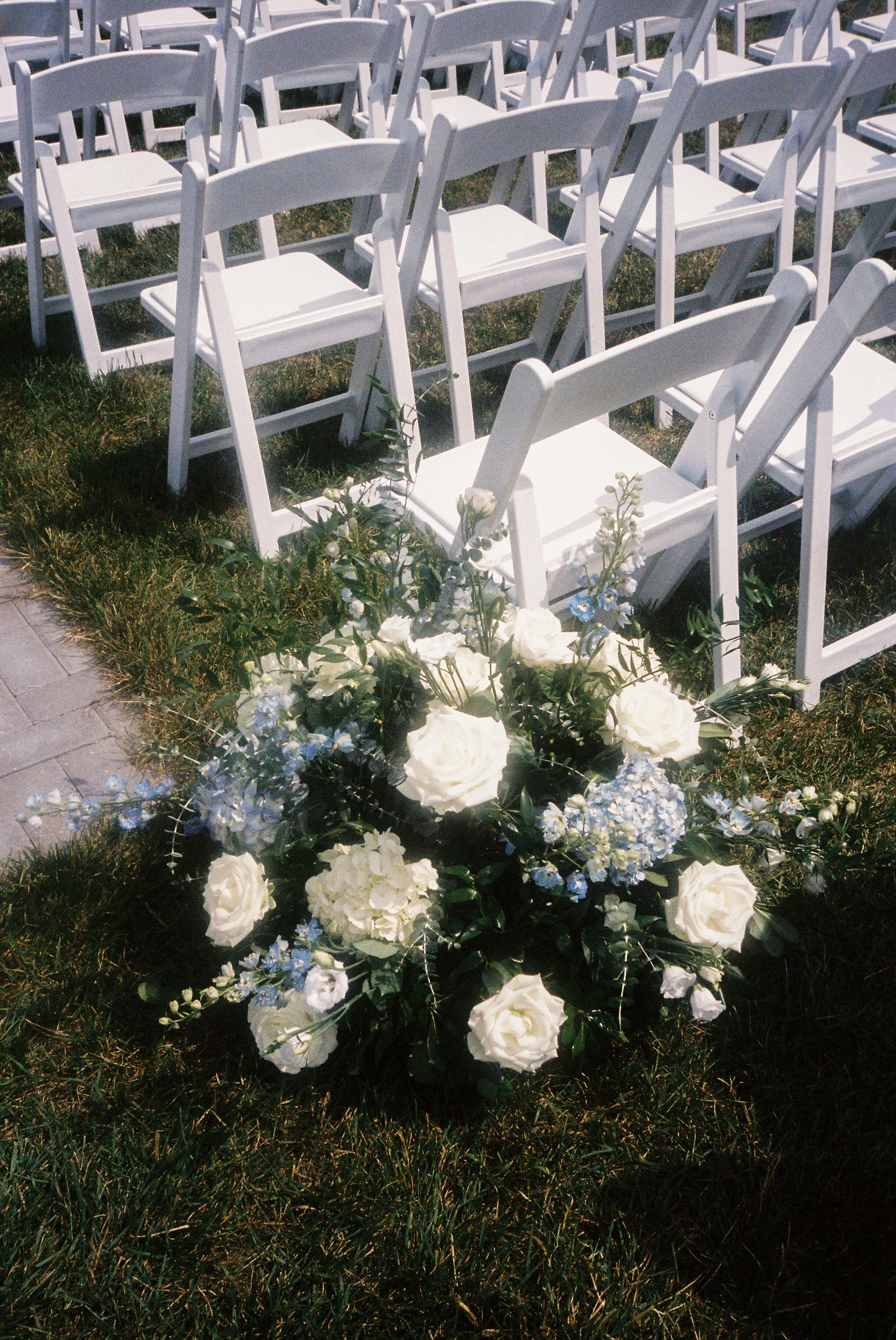 White and blue ceremony aisle flowers arranged beside rows of white chairs at an outdoor Northern Michigan vineyard wedding ceremony.