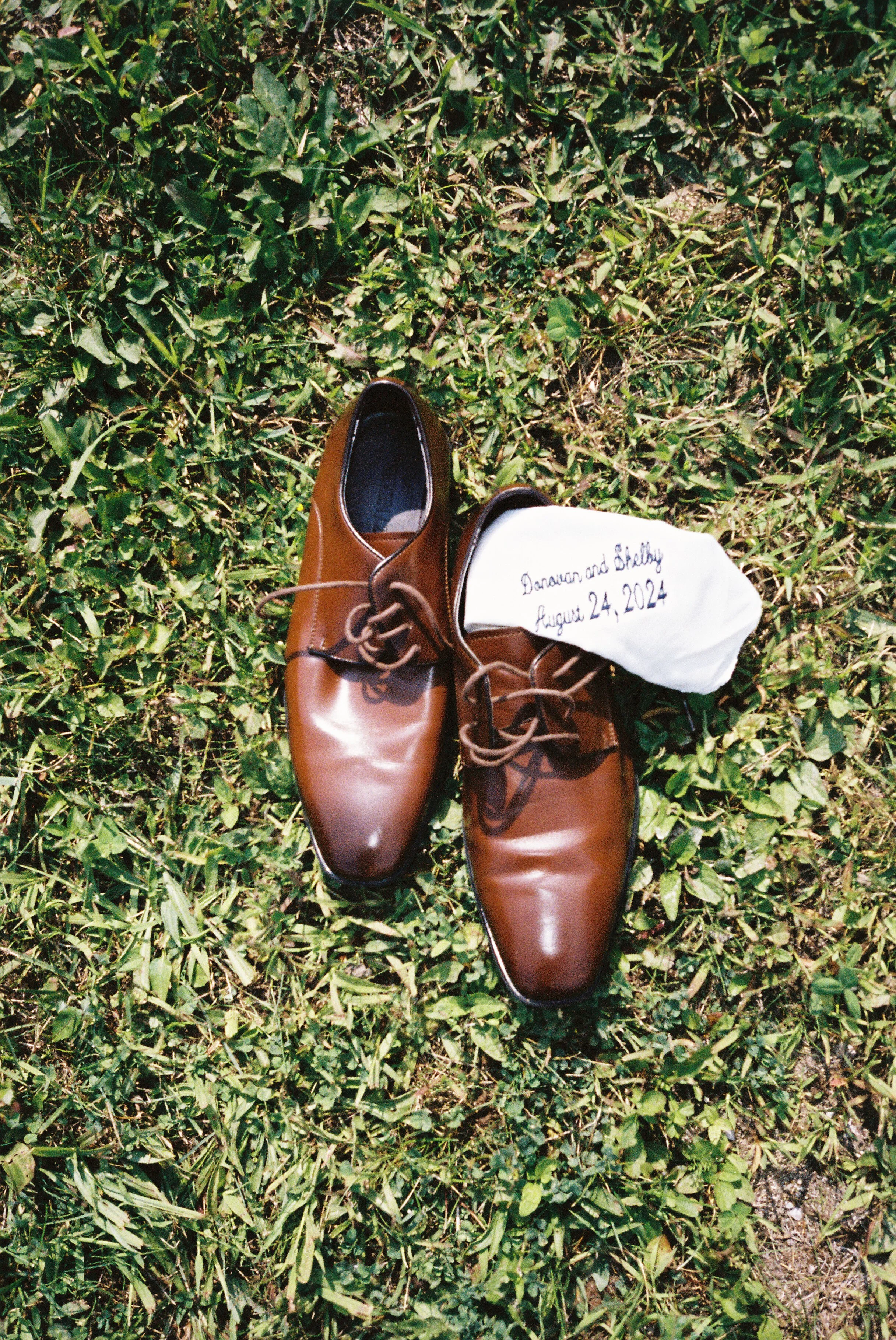 Brown groom's wedding shoes and embroidered handkerchief displayed on the grass before a Northern Michigan vineyard wedding.