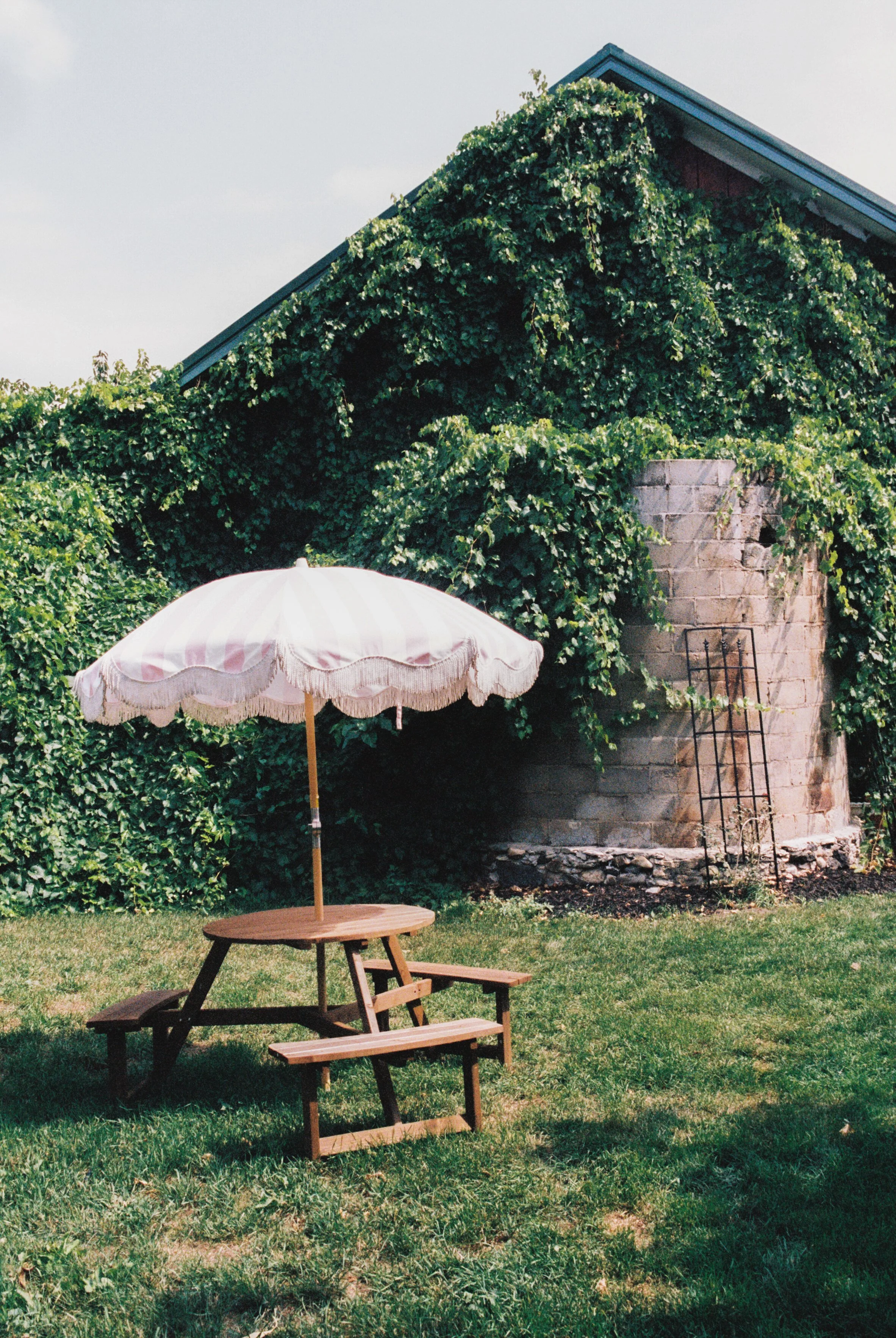 Vintage-inspired seating area with a fringed parasol and picnic table surrounded by vineyard greenery at a Northern Michigan wedding venue.