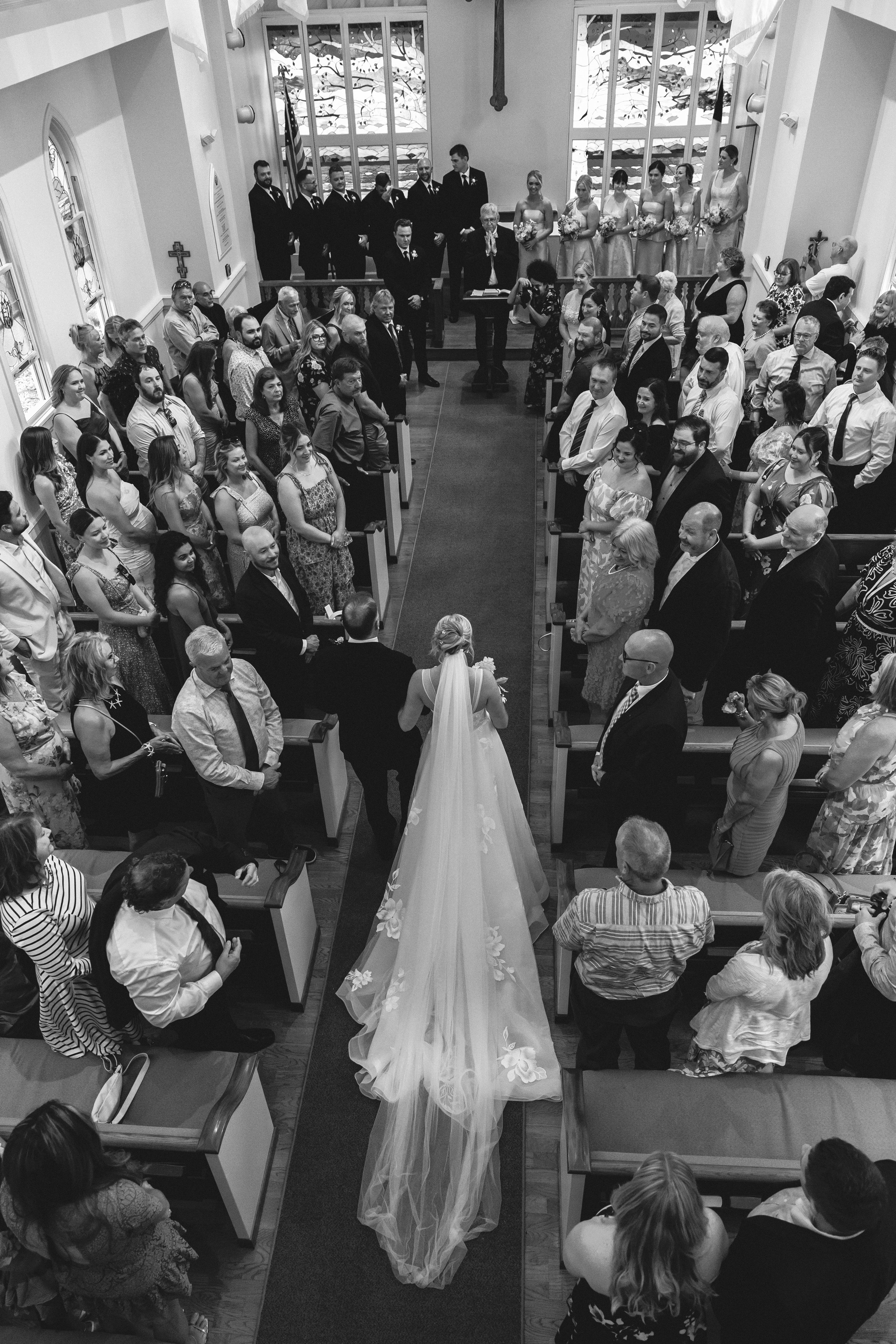 Black and white photo of a bride and groom walking down the church aisle surrounded by family and friends.