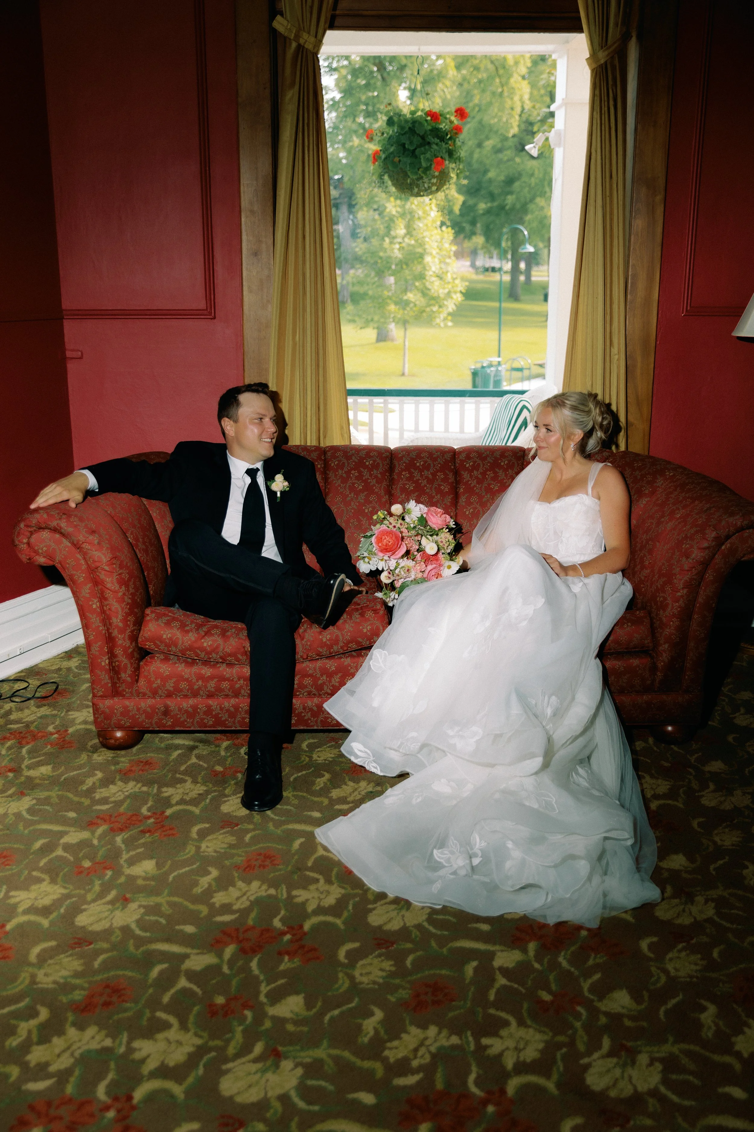 Bride and groom relaxing together on a vintage red couch during their wedding day portraits at Stafford's Perry Hotel.