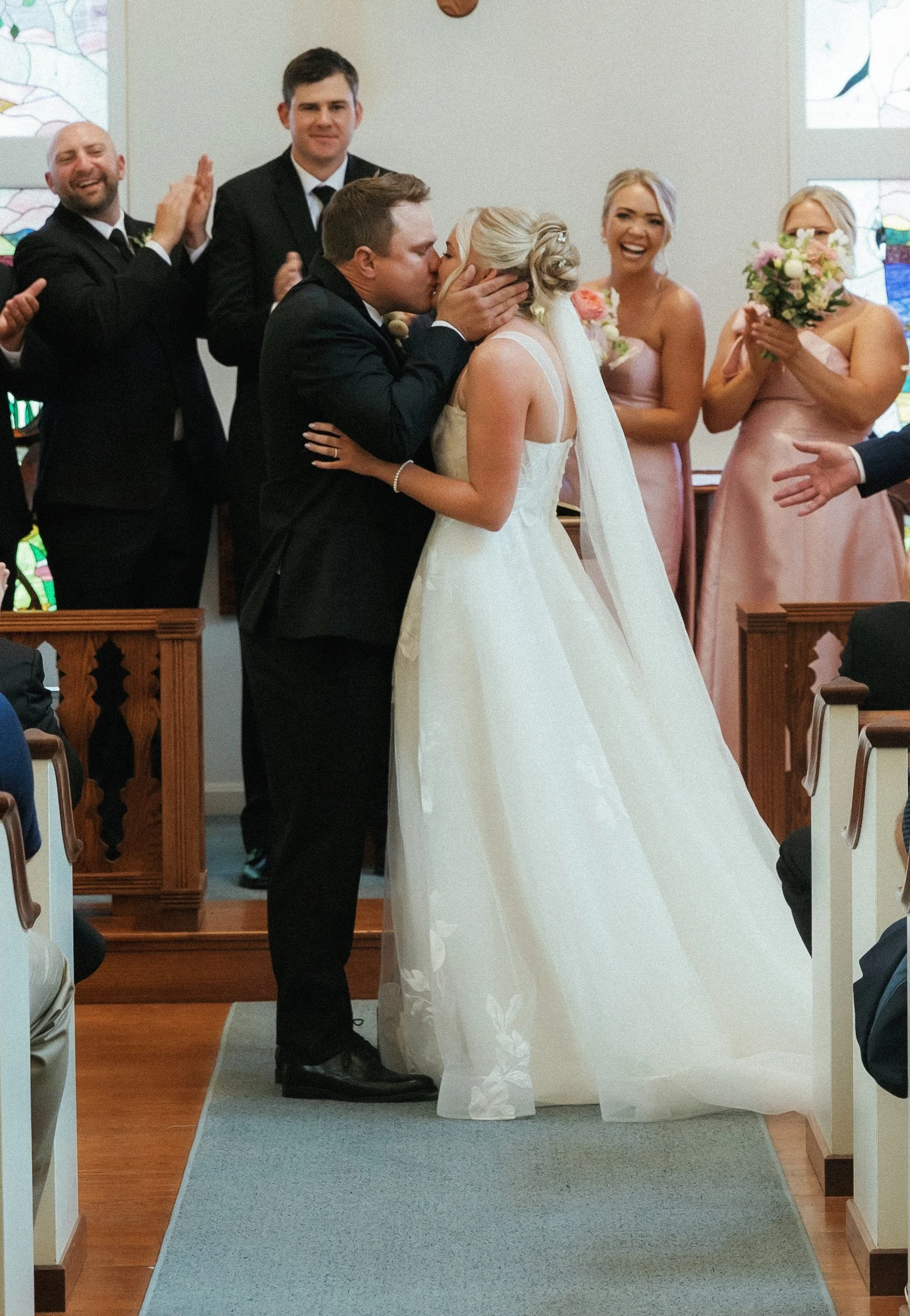Bride and groom sharing their first kiss during the wedding ceremony surrounded by their wedding party at Stafford's Perry Hotel.