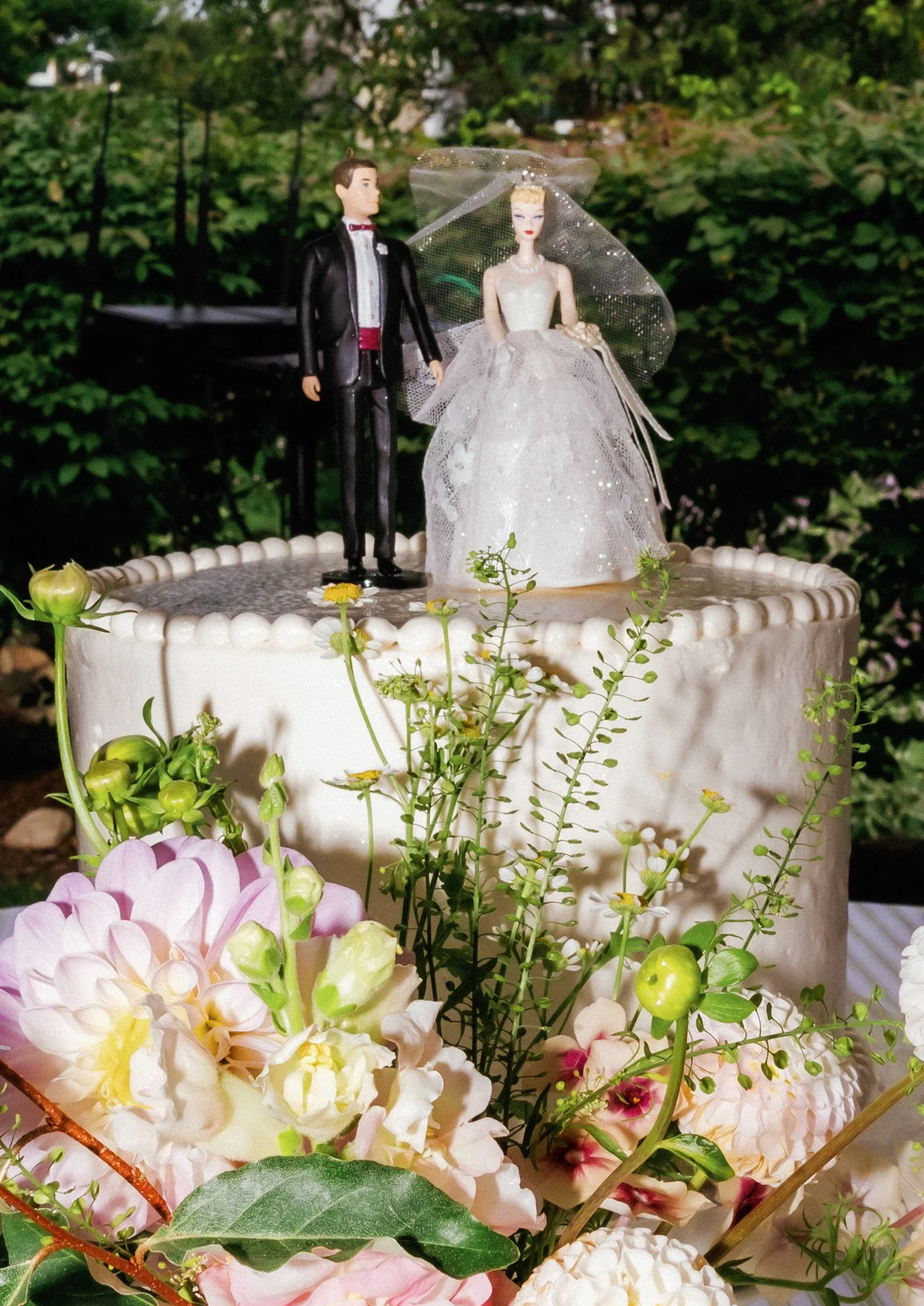 Vintage-inspired wedding cake topped with a bride and groom figurine surrounded by fresh flowers.