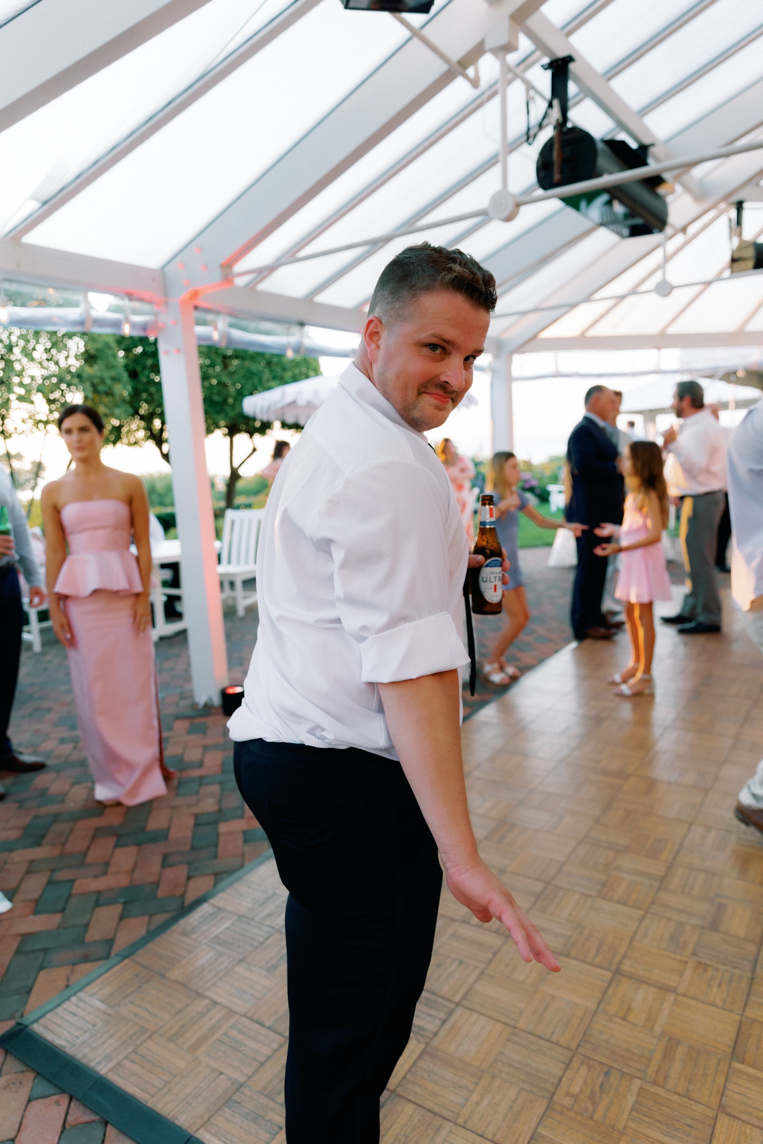 Wedding guest dancing on the reception dance floor with a drink in hand during the celebration.