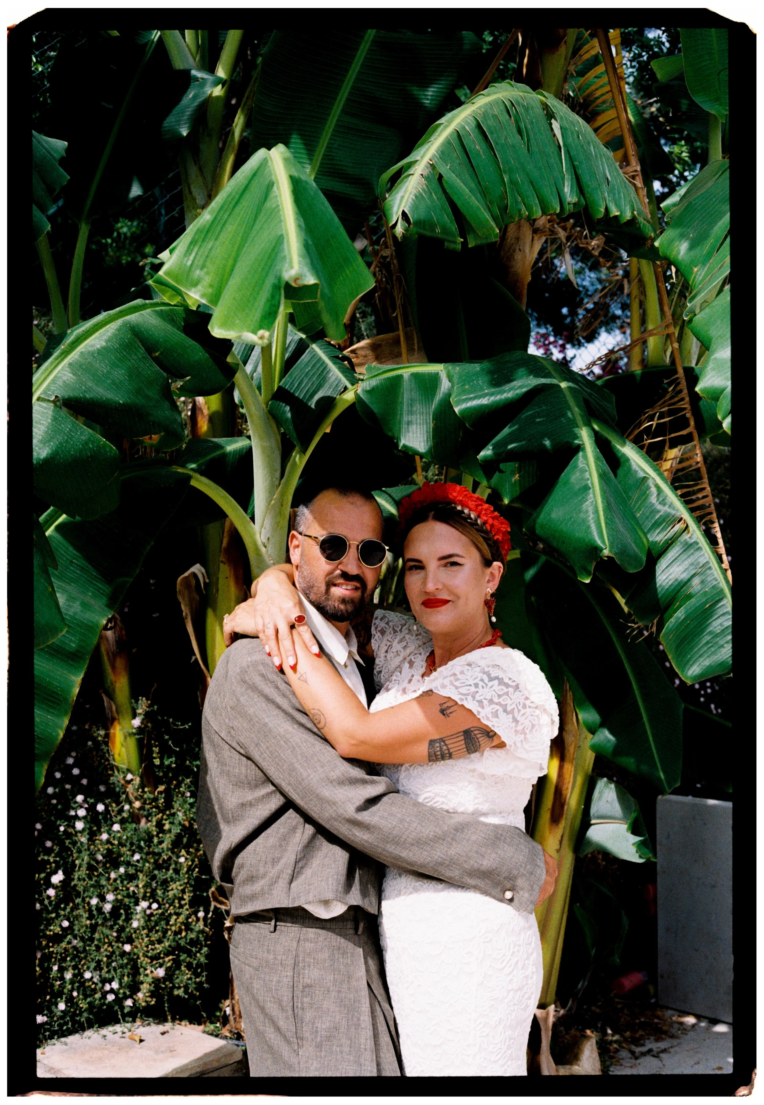 Couple embracing beneath lush tropical greenery during their Spain wedding celebration.