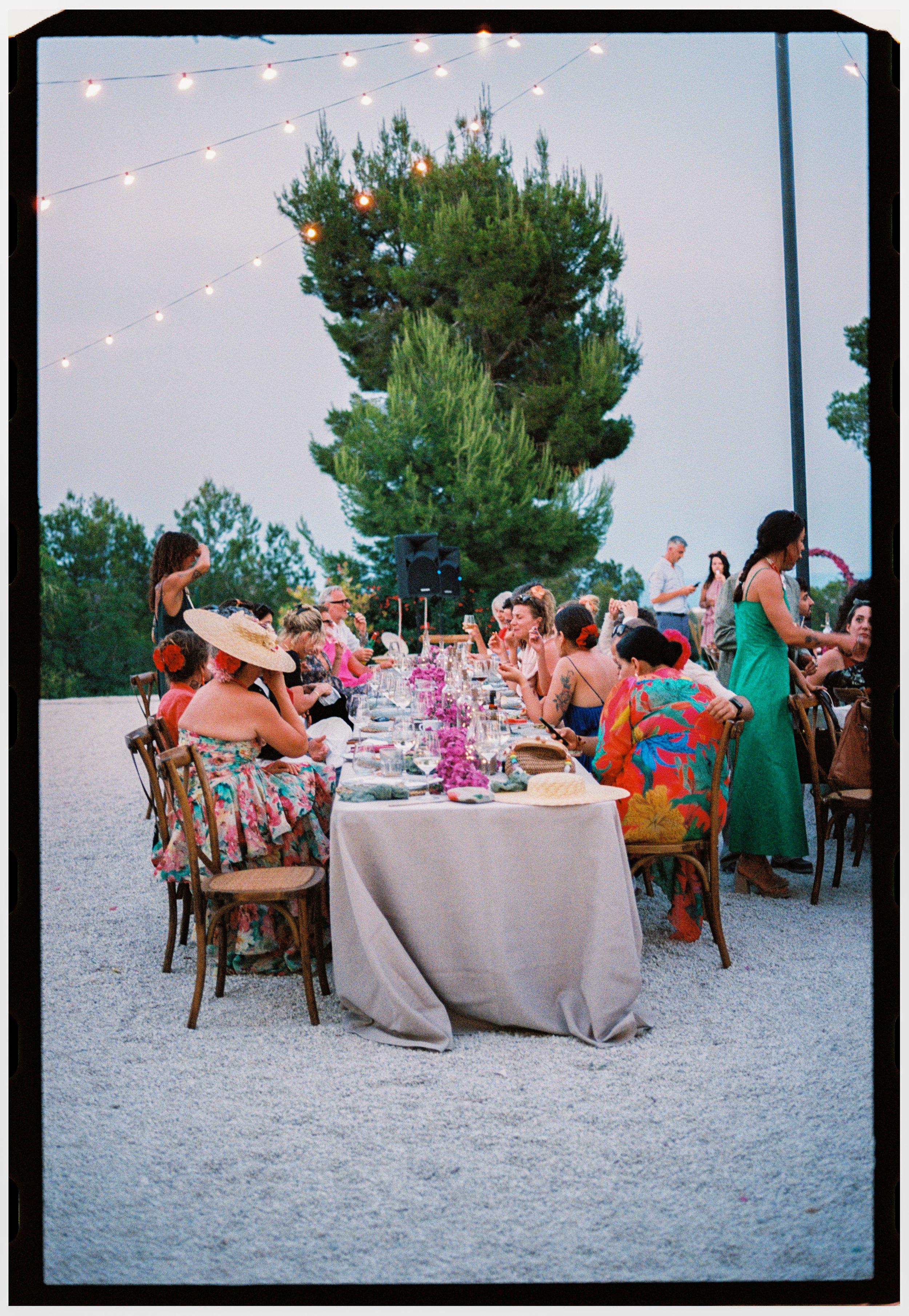 Guests gathered around long reception tables beneath string lights for an outdoor wedding dinner.