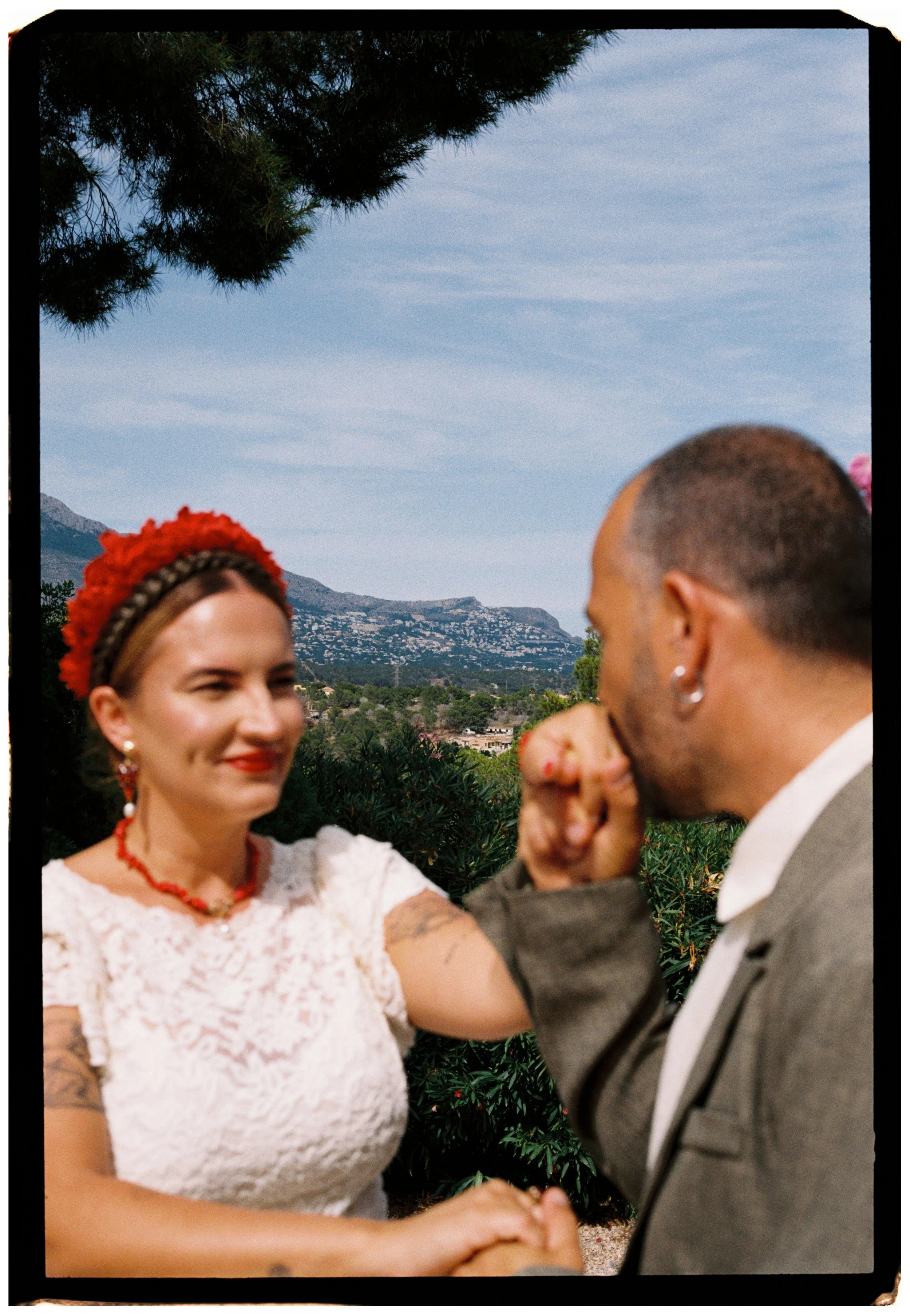 Groom kissing the bride's hand with scenic mountain views in the background during their Spain wedding.