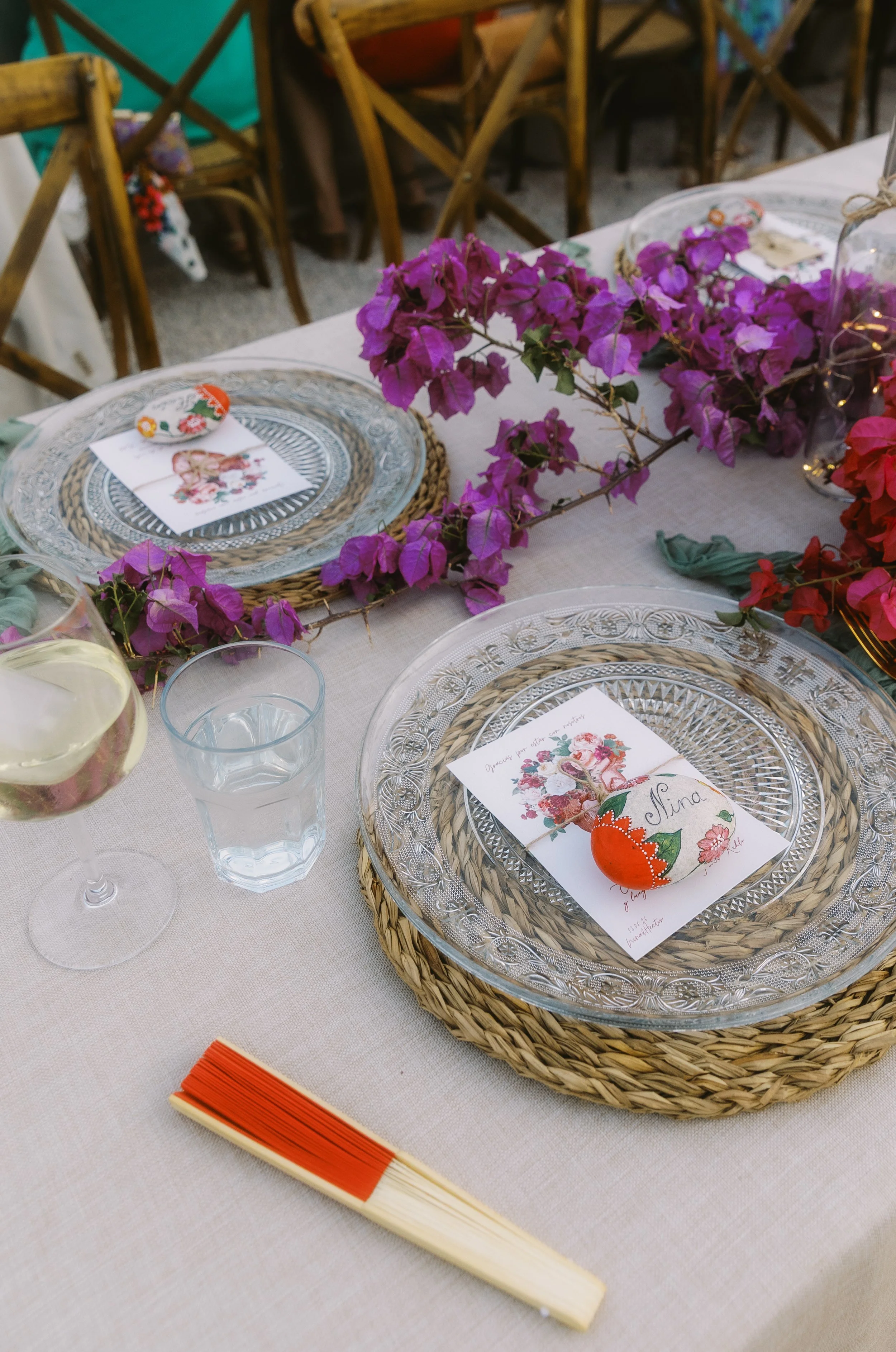 Reception place setting with woven chargers, vibrant bougainvillea, and colorful wedding stationery.