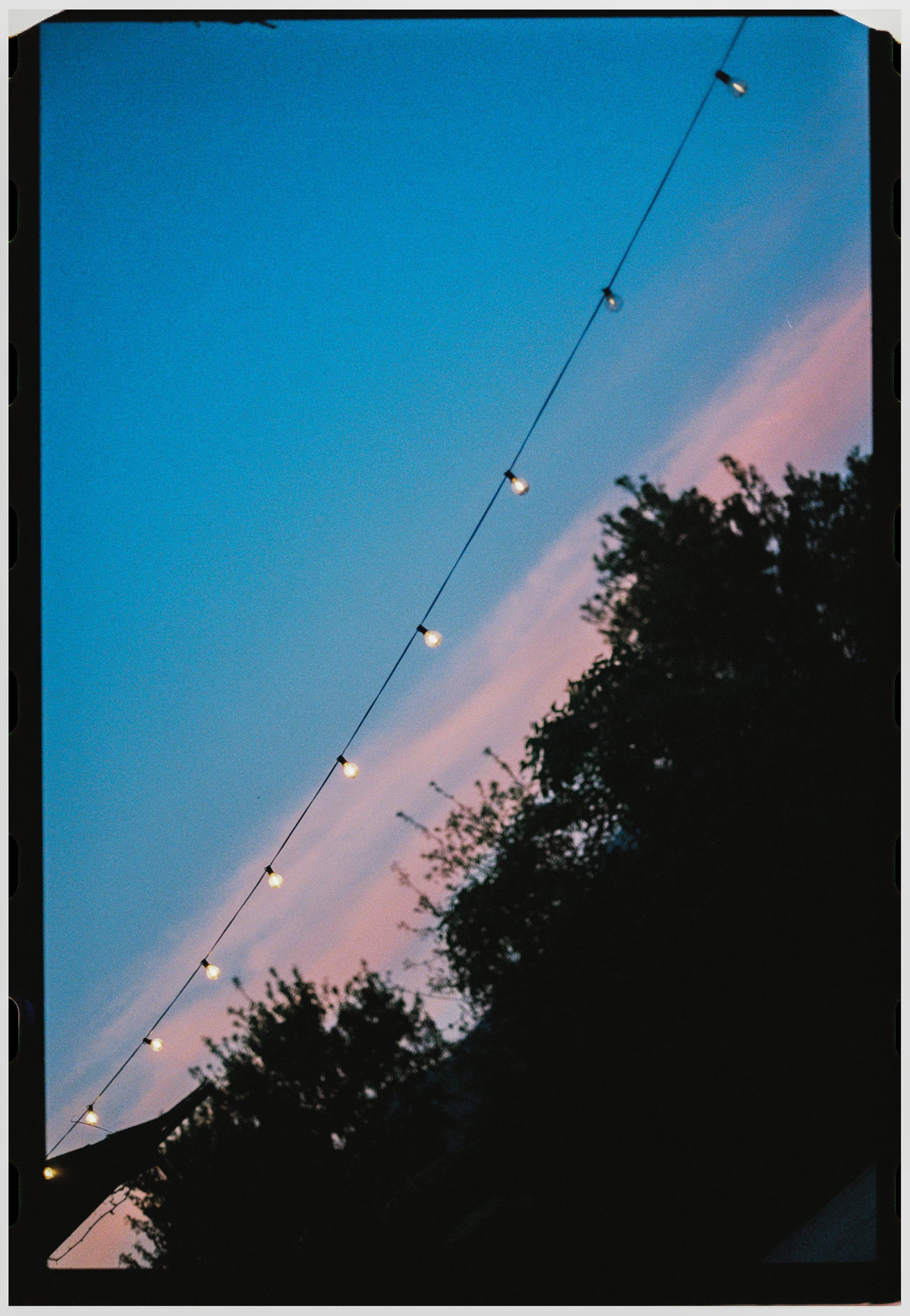 String lights glowing against a colorful evening sky above the wedding venue.