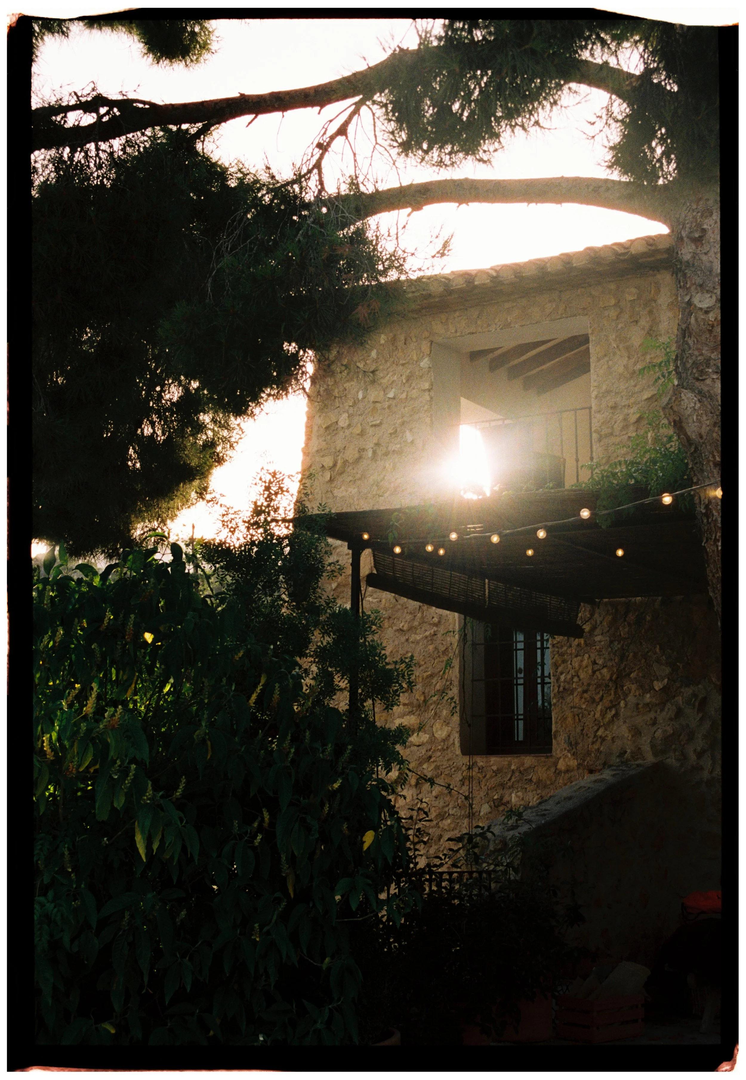 Golden sunset shining through a rustic stone villa decorated with string lights.