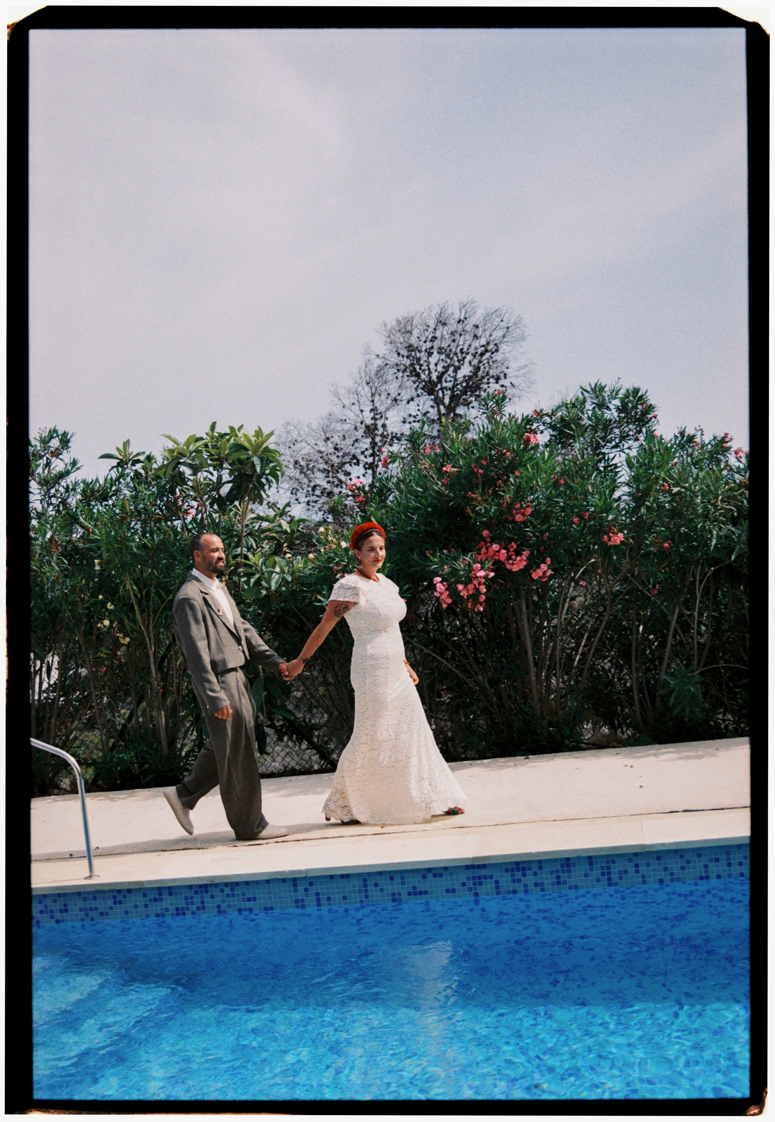 Newlyweds walking hand in hand beside a pool during their Spain wedding.