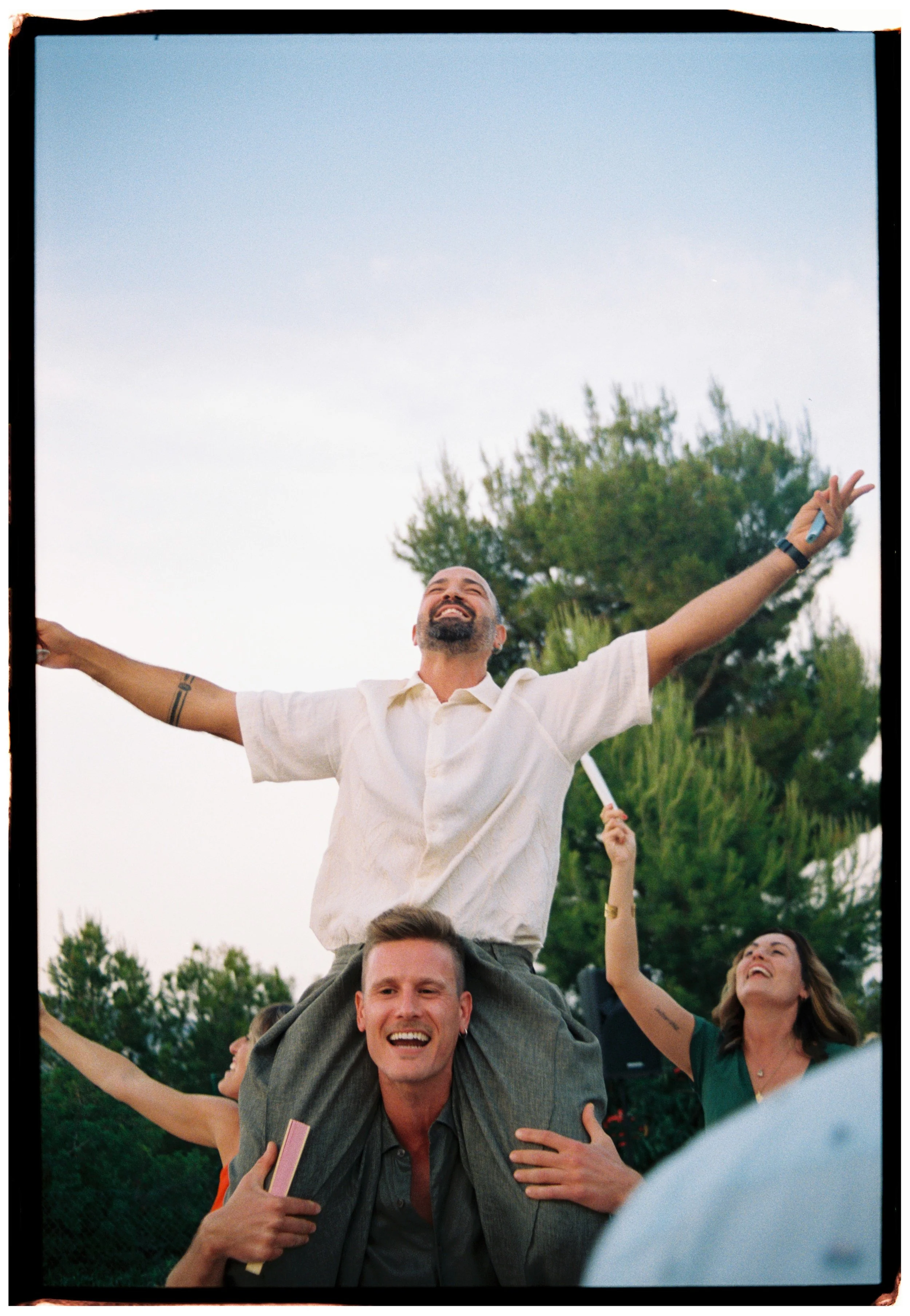 Groom celebrating on friends' shoulders during the outdoor wedding reception.