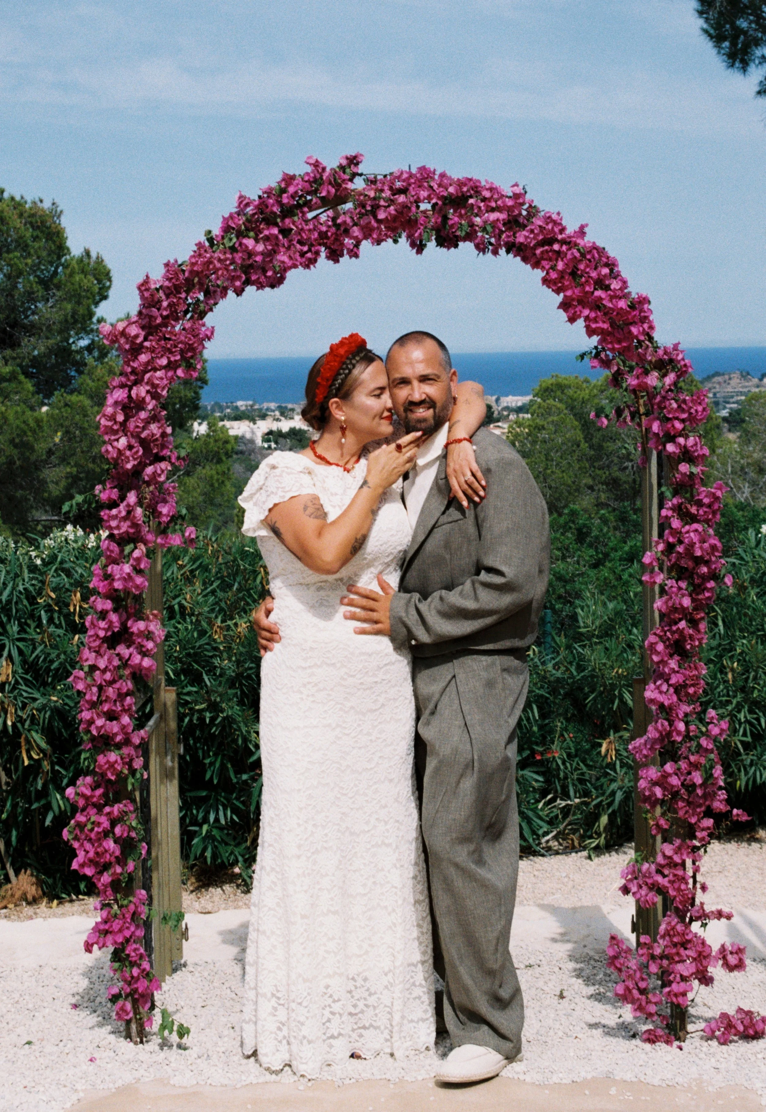 Bride and groom embracing beneath a vibrant pink floral arch during their Spain wedding.