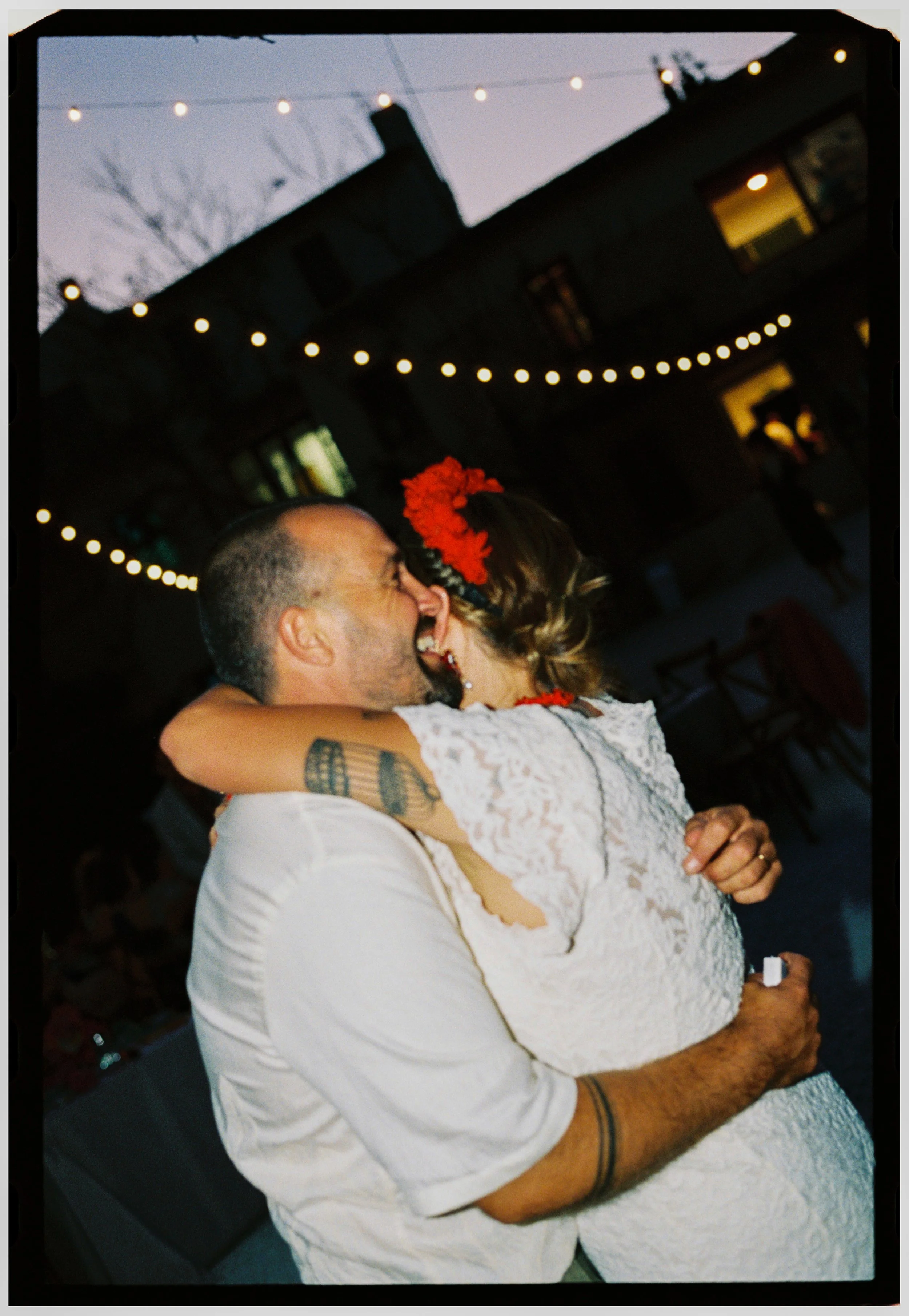 Bride and groom embrace each other while dancing under string lights