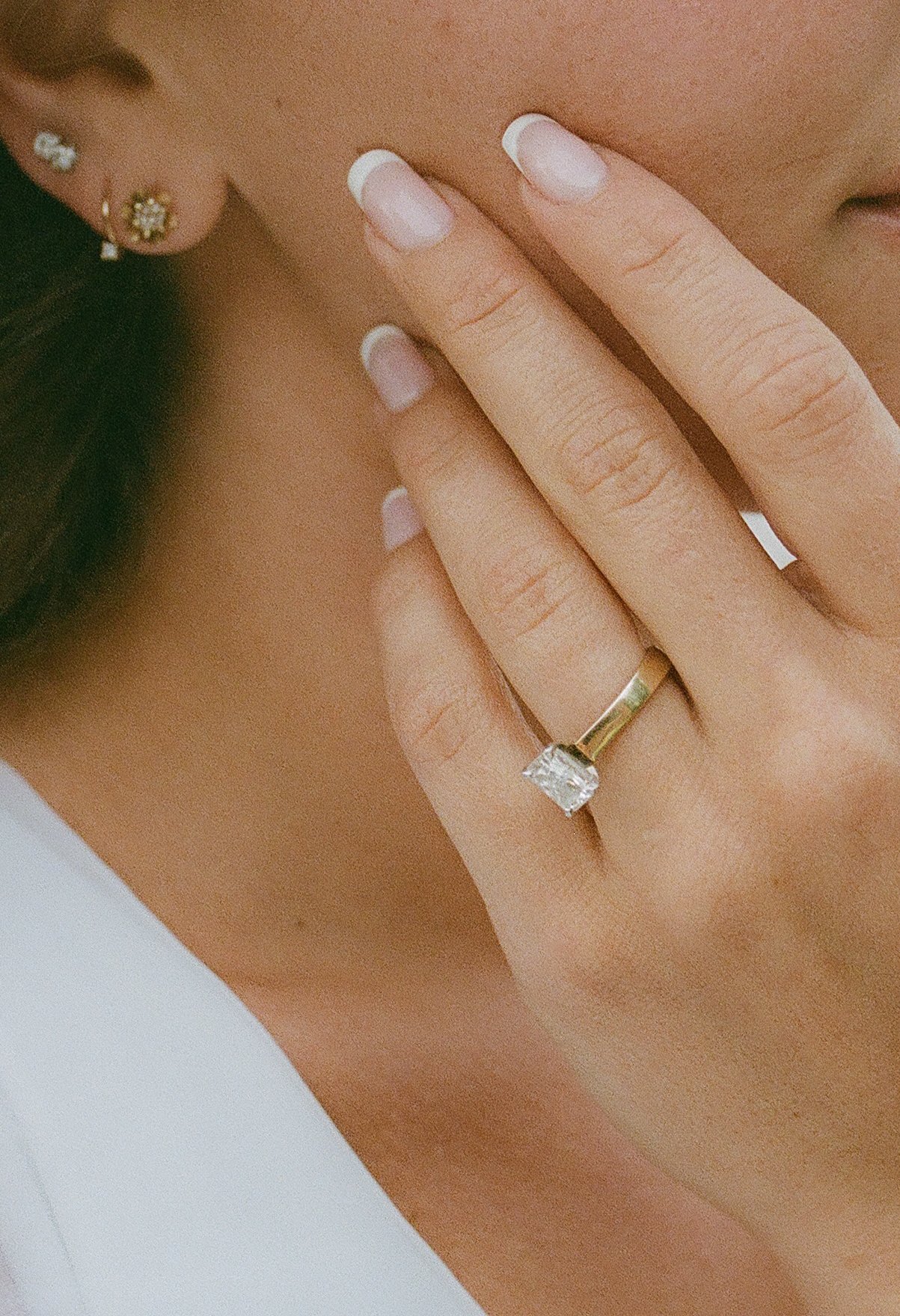 Close-up of a radiant-cut diamond engagement ring on a gold band worn by the bride.