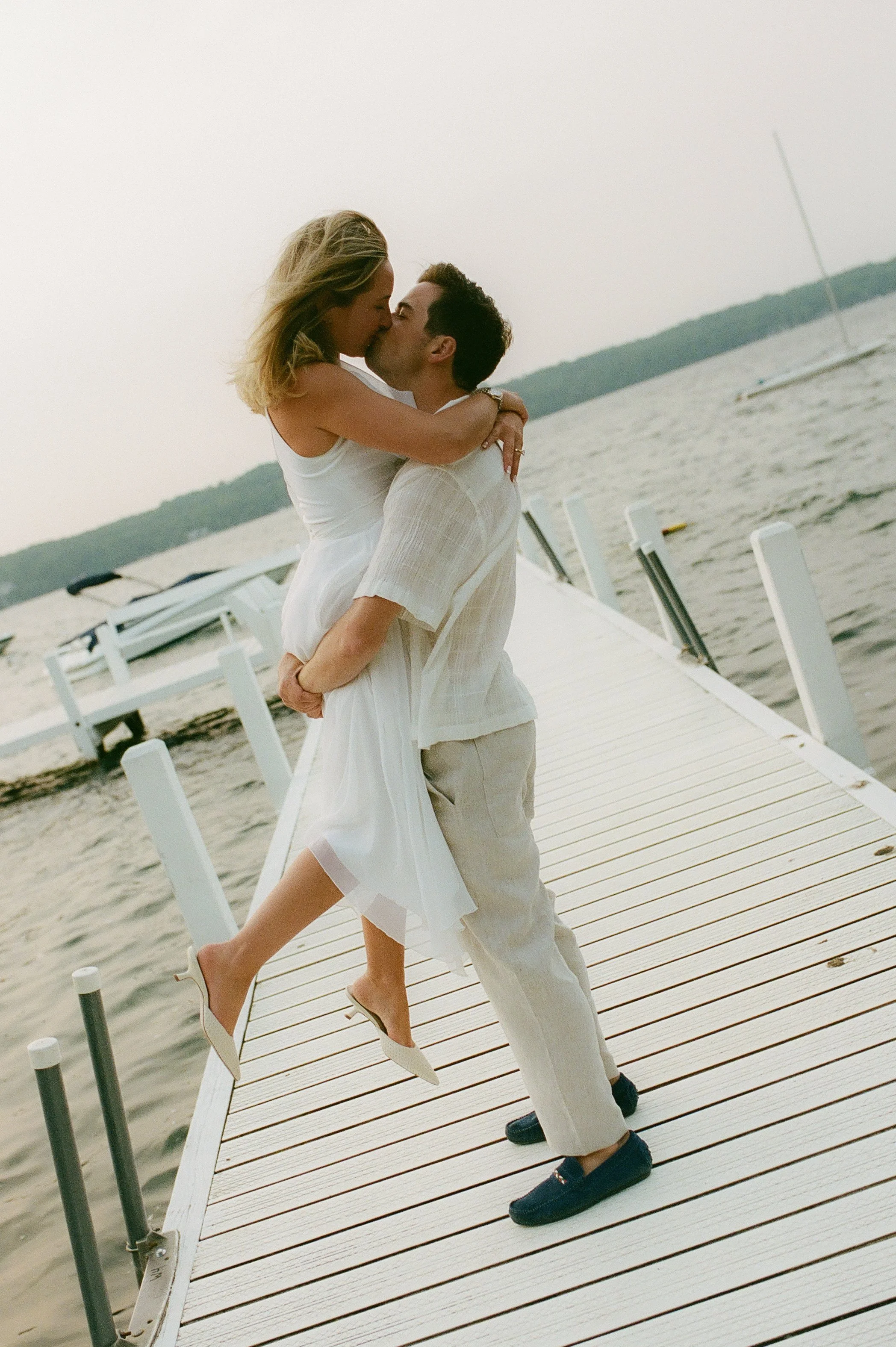 Couple embracing and kissing on a lakeside dock during their Lake Geneva Engagement session at golden hour.