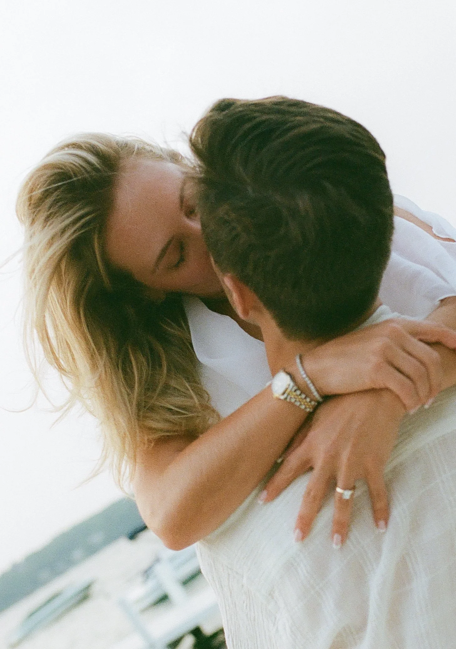 Close-up of an engaged couple sharing an intimate embrace and kiss with the engagement ring visible.