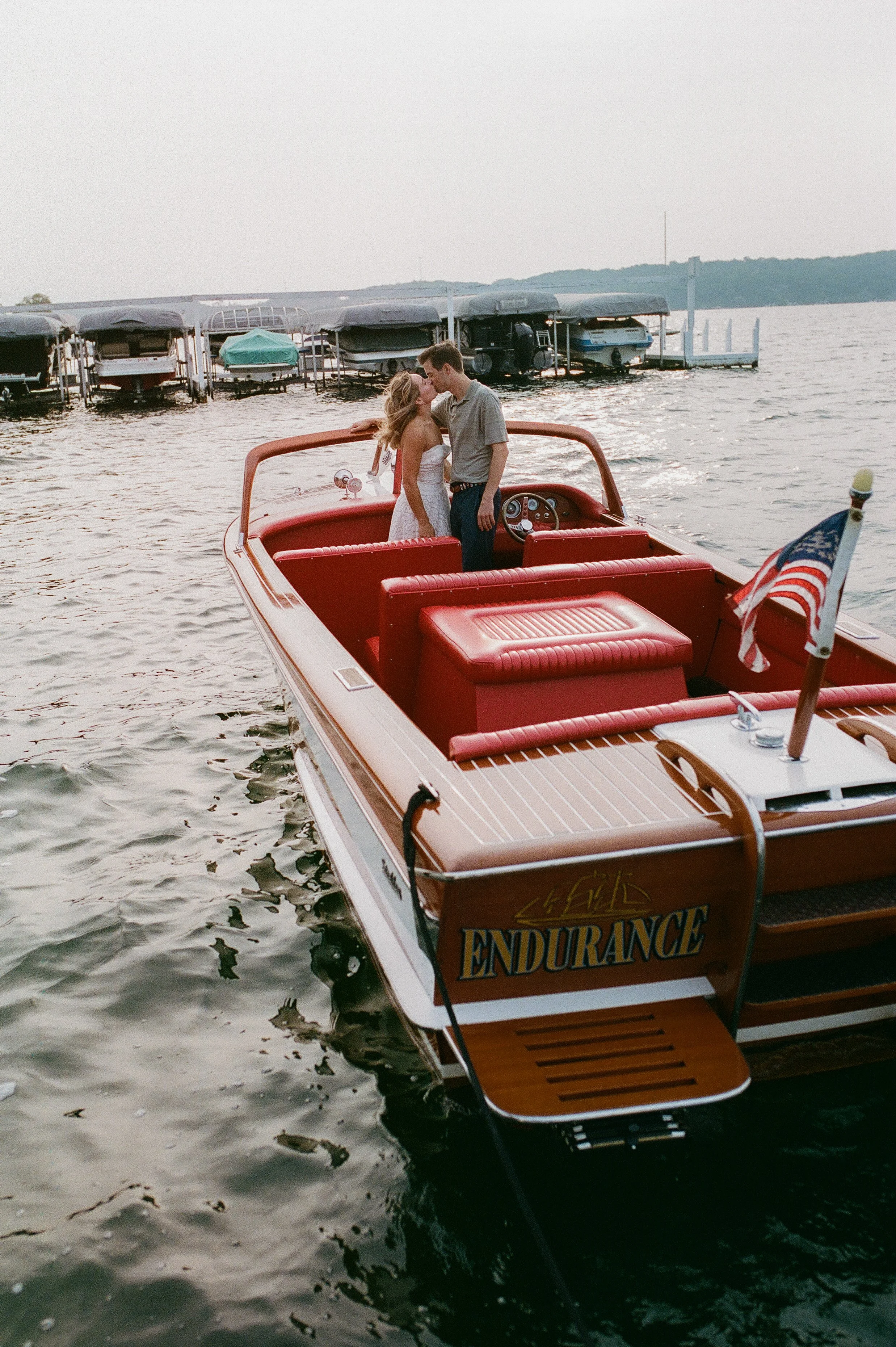 Couple kissing aboard a vintage wooden boat with bright red leather seating on Lake Geneva.