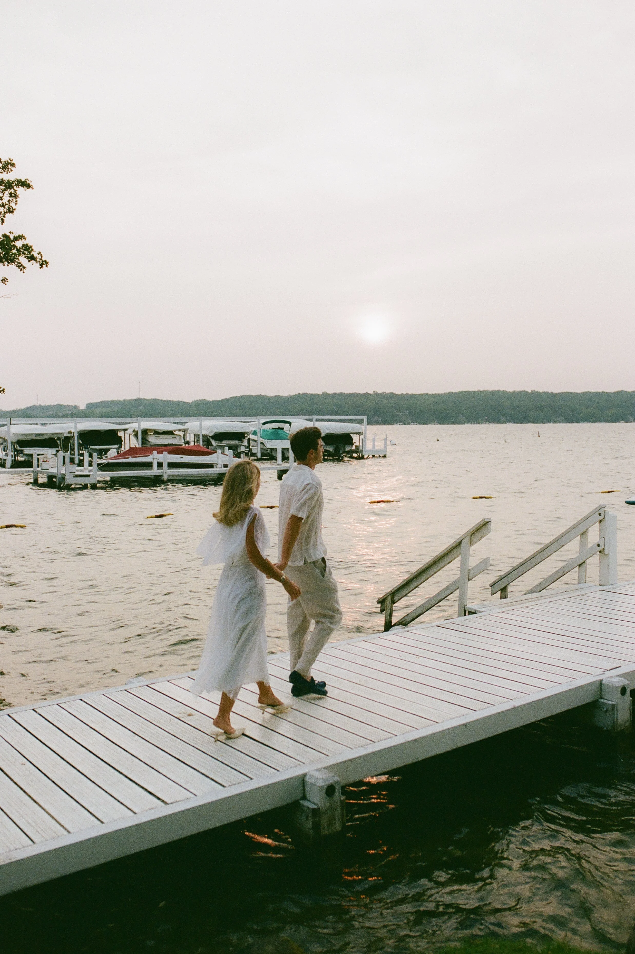 Couple walking hand in hand along the dock as the sun sets over Lake Geneva during their Lake Geneva Engagement session.